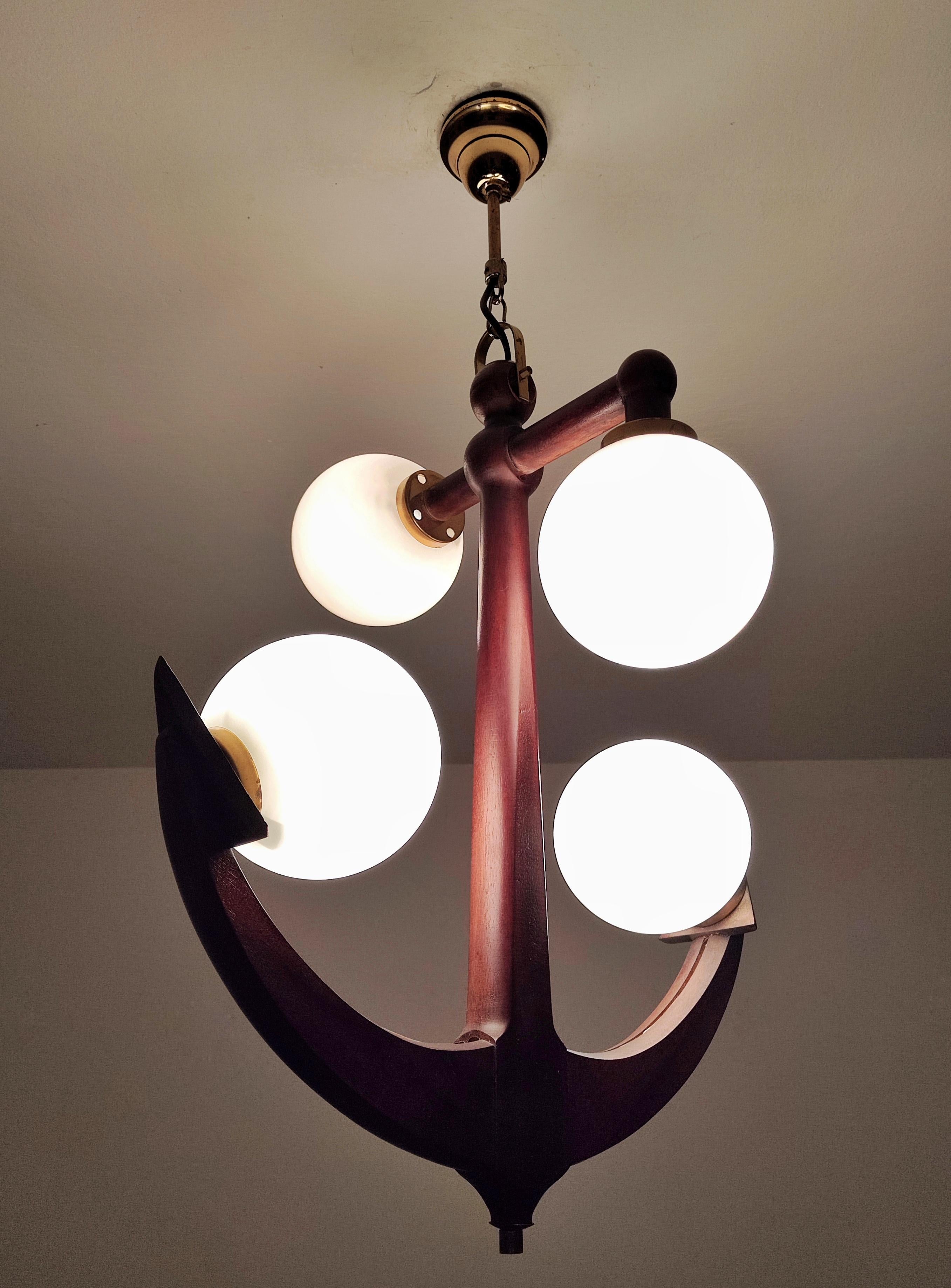 In this listing you will find a spectacular and extremely rare Mid Century Modern light pendant shaped as anchor. It is done in solid mahogany, making this piece very luxurious. It features 4 opaline glass balls shades that provide very soft and