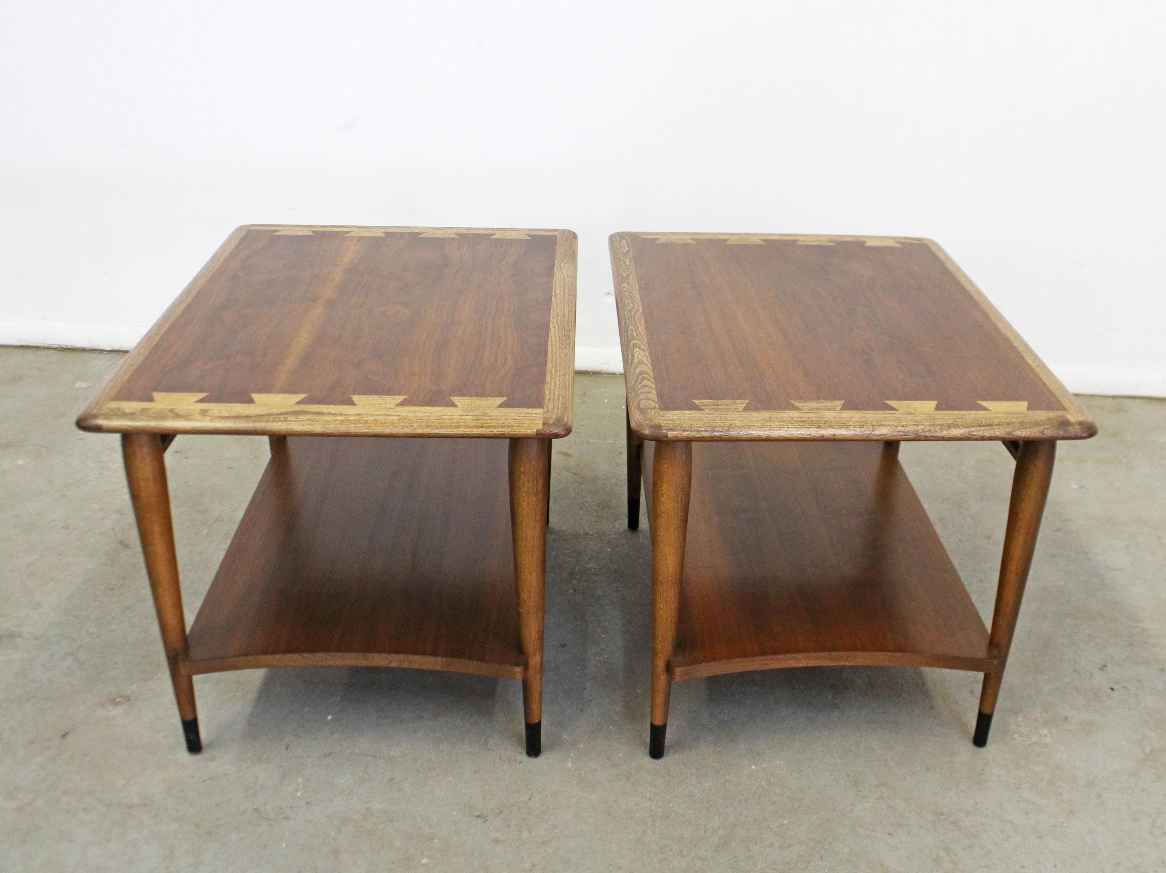 Offered is a pair of Mid-Century Modern end tables from the Lane 'Acclaim' collection, designed by Andre Bus. They have the signature dovetailed design and tapered legs and bottom shelves. They each have an oak edge with a walnut top and walnut