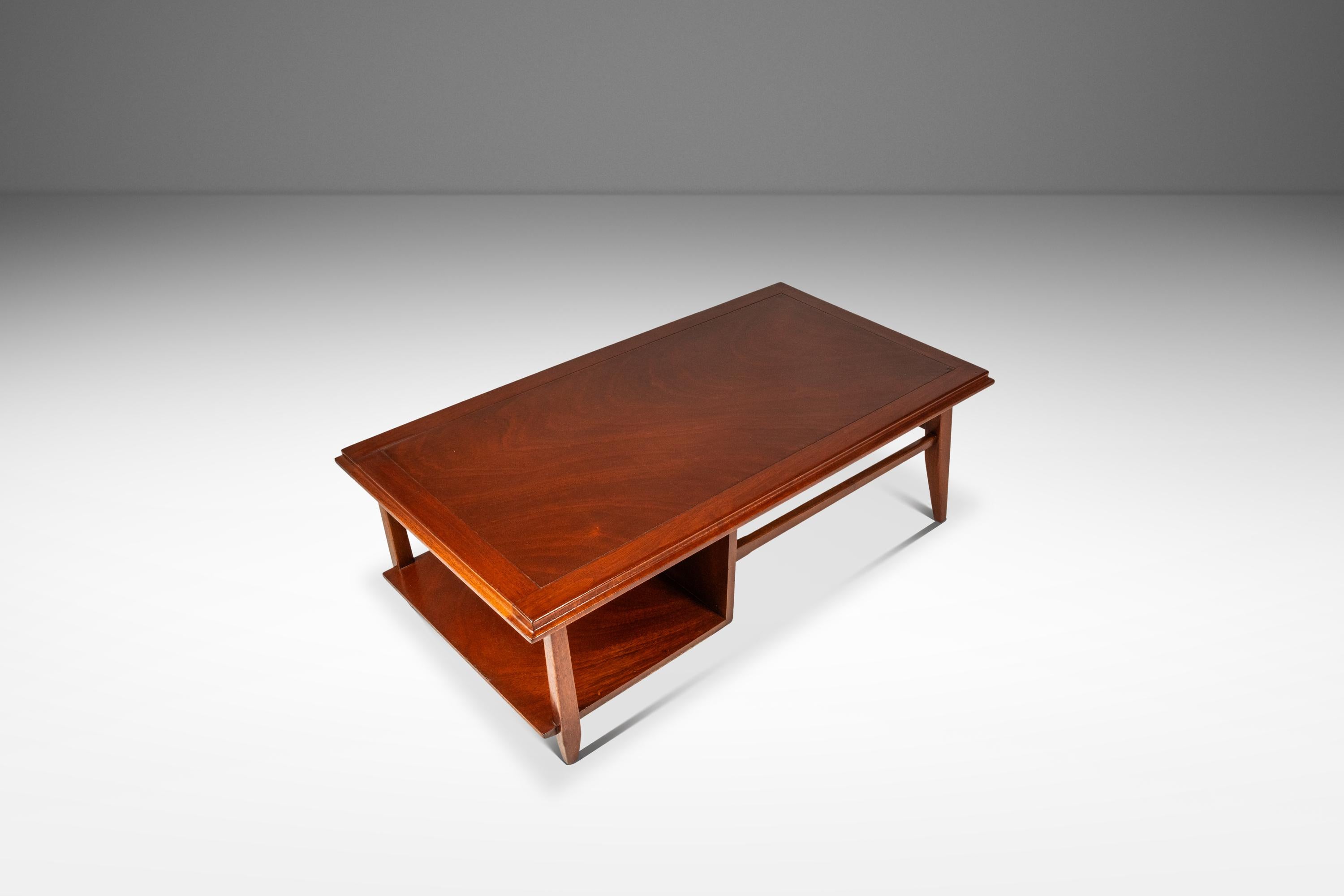 This sophisticated Mid-Century Modern coffee table, crafted in the 1960s, showcases the era’s elegant design with its rich mahogany construction and distinctive beveled edge. The warm, reddish-brown tones of the mahogany highlight its smooth grain,