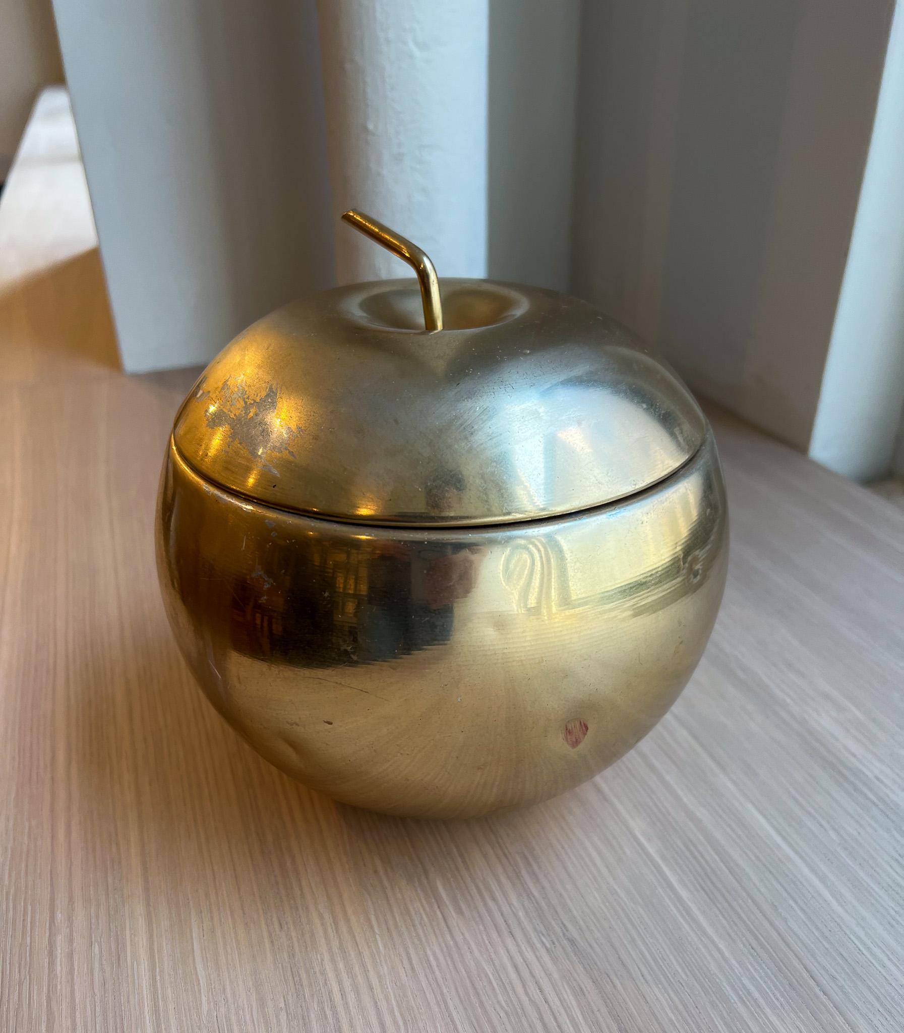 This mid-century modern apple ice bucket is made with a metal exterior and cream plastic interior. The metal has been newly polished, but shows moderate wear as shown in the images. The ice bucket has a sleek and elegant look and can be styled into
