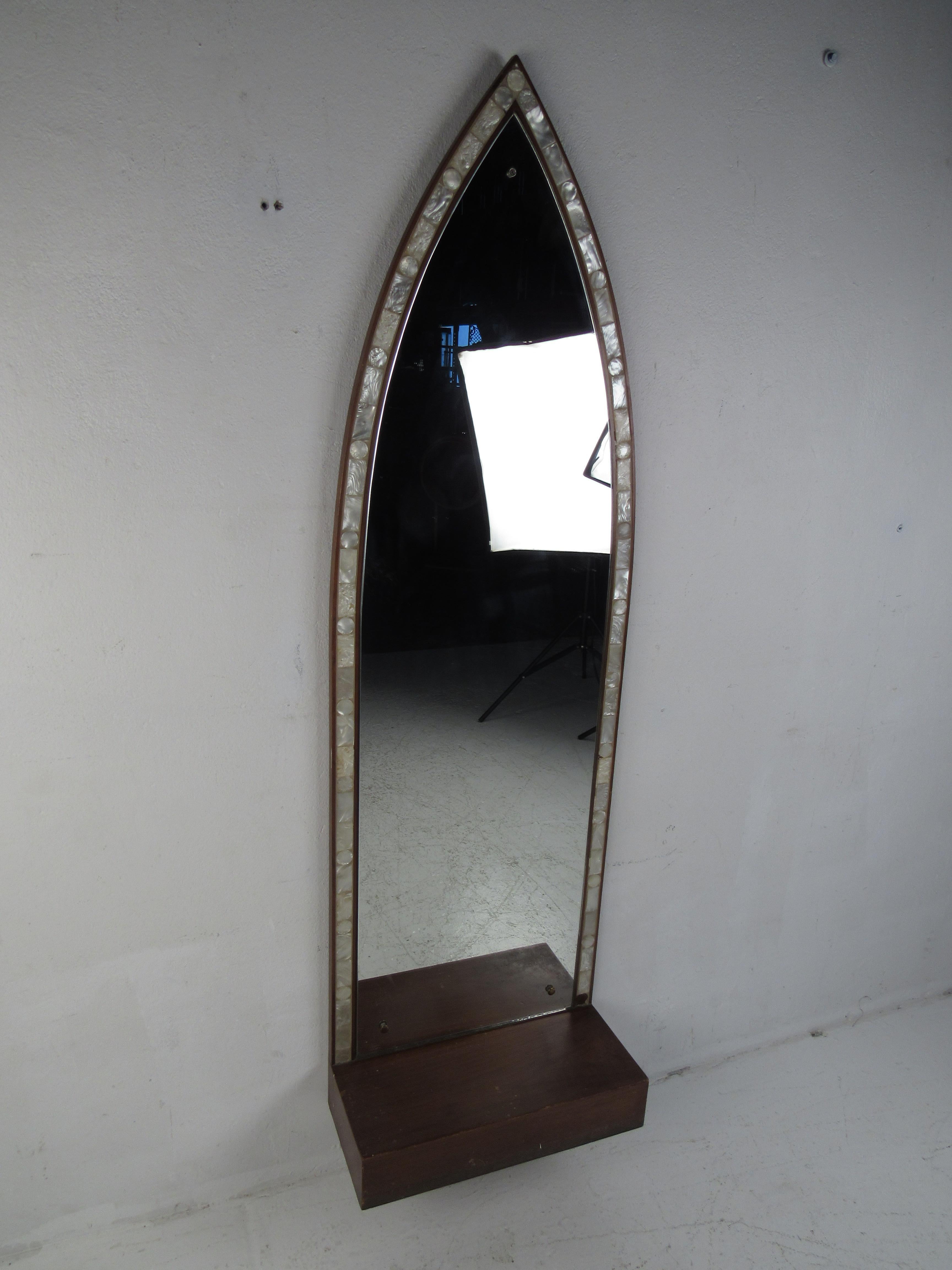 This stunning vintage modern mirror features an unusual textured trim resembling mother of pearl around the edges. The beautiful decorative inlay, unique arched top, and thick walnut shelf adds to the mid-century appeal. A wonderful design that