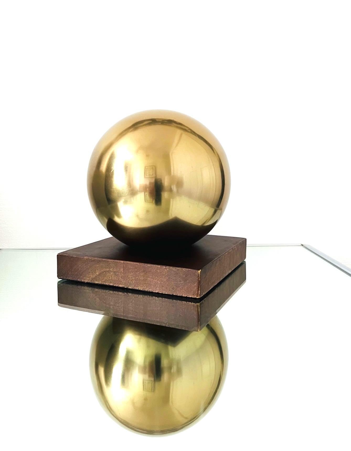 Mid-Century Modern polished brass ball orb sculptural bookend. The design features a round spherical globe beautifully enhanced by a square walnut wood Stand, adding an architectural element to any room. The base is stained in a walnut brown finish.