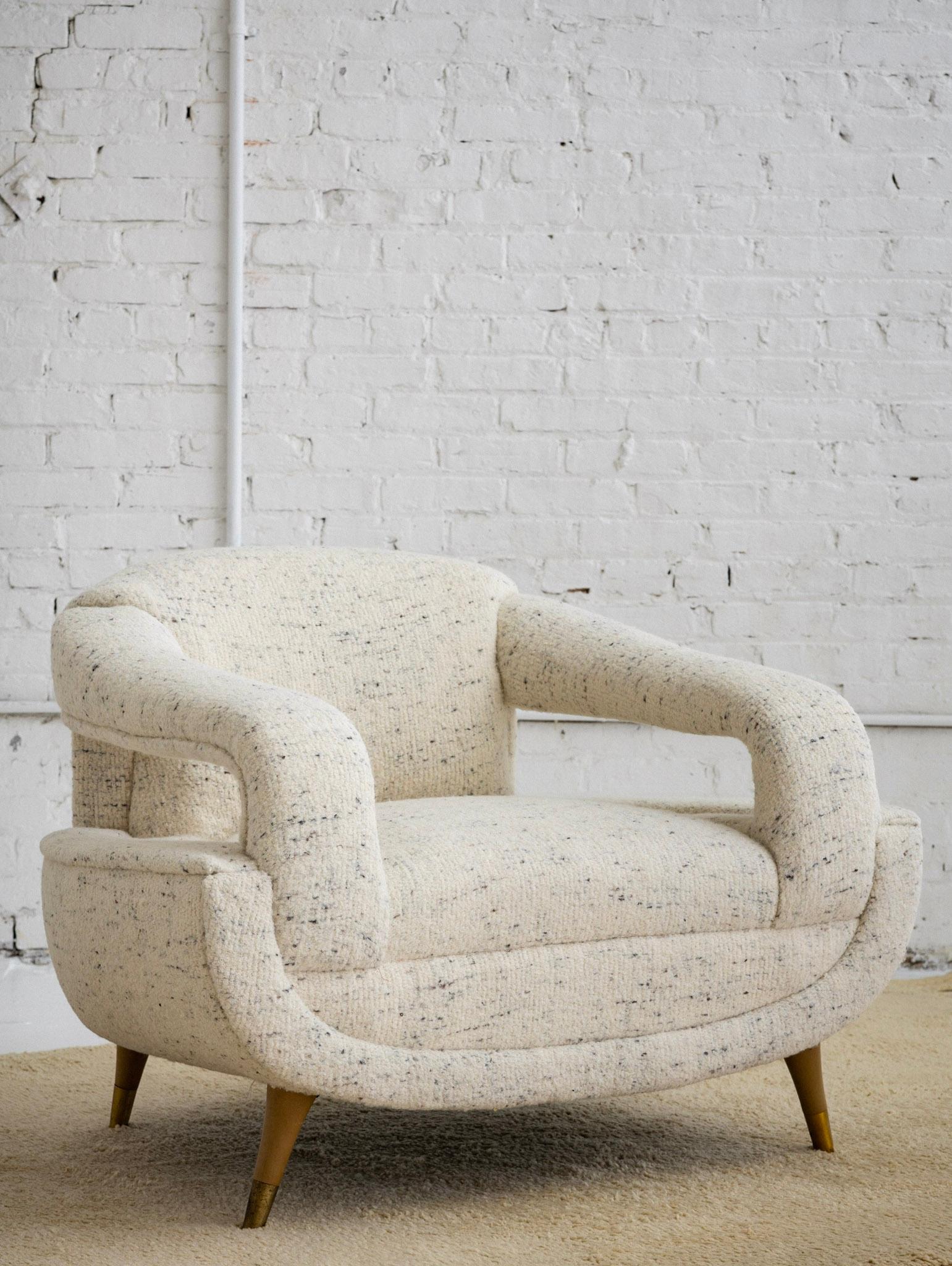 A Mid-Century Modern armchair. Newly reupholstered in a soft textured wool. Cream in color with speckles of brown and black. Blonde wood feet with brass caps.