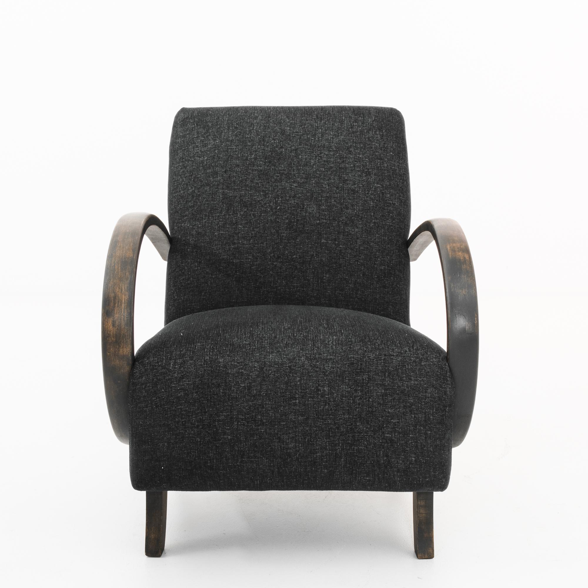 A bentwood upholstered armchair by Czech furniture designer J. Halabala, circa 1960. A Mid-Century Modern silhouette, upholstered in dark grey twill. The cushioned seat is parenthesized by the dramatic swoop of the wooden armrests; the curves of the