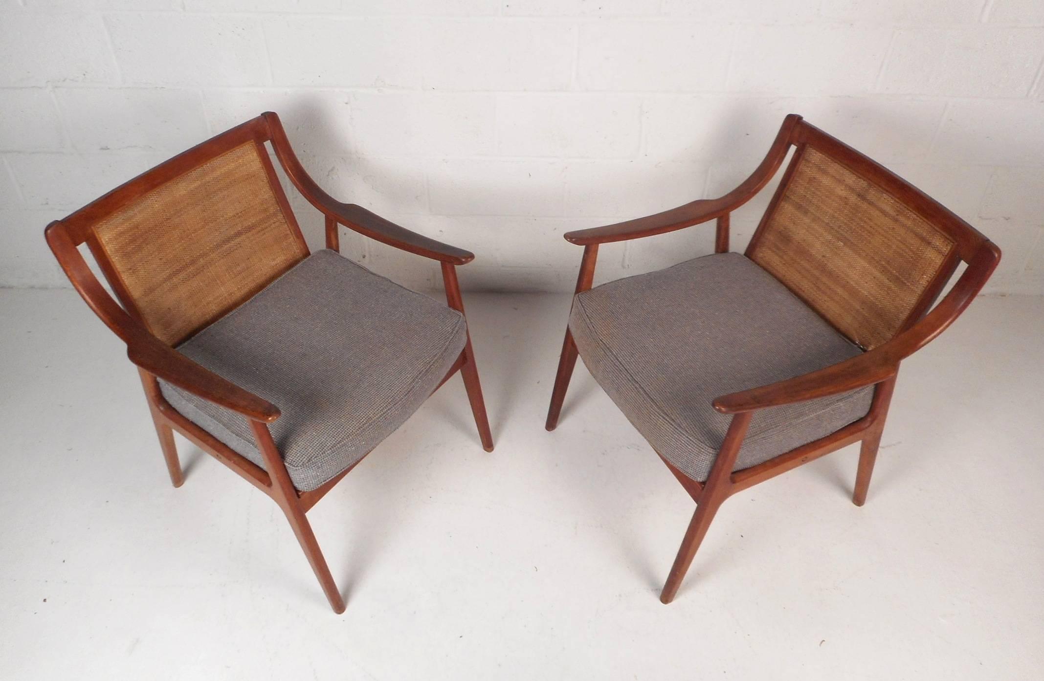 A stunning pair of vintage modern lounge chairs with cane back rests and a removable cushion. This Danish style pair feature sloping arm rests, a woven cane back rest, and angled legs. Sturdy walnut frames and a thick upholstered cushions show