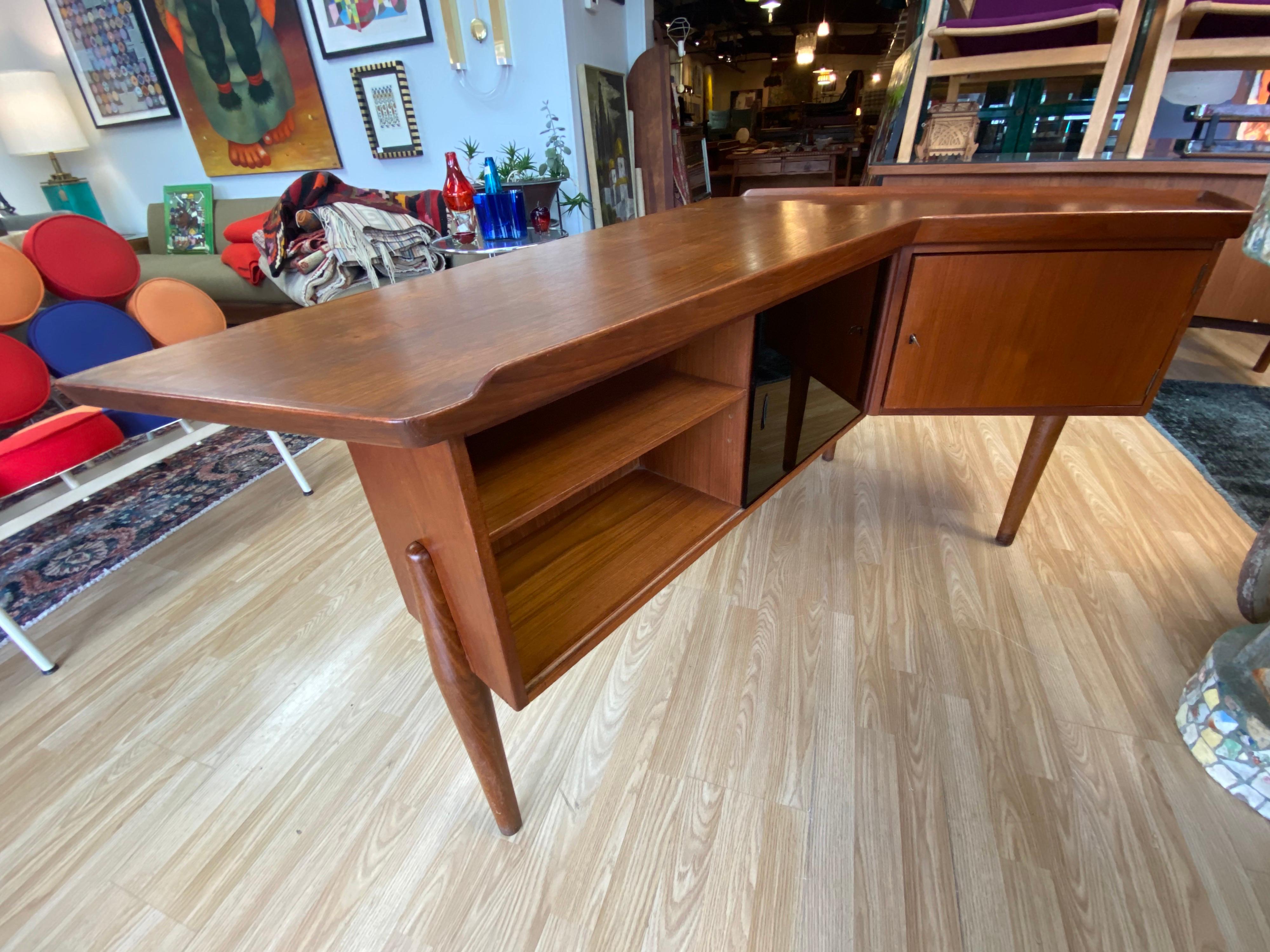 Unique Mid-Century Modern teak desk designed by Arne Hovmand-Olsen features a boomerang shape, three drawers with inset teak pulls and the backside features two shelves for storage, a sliding ebonized door that opens up to more storage, and a