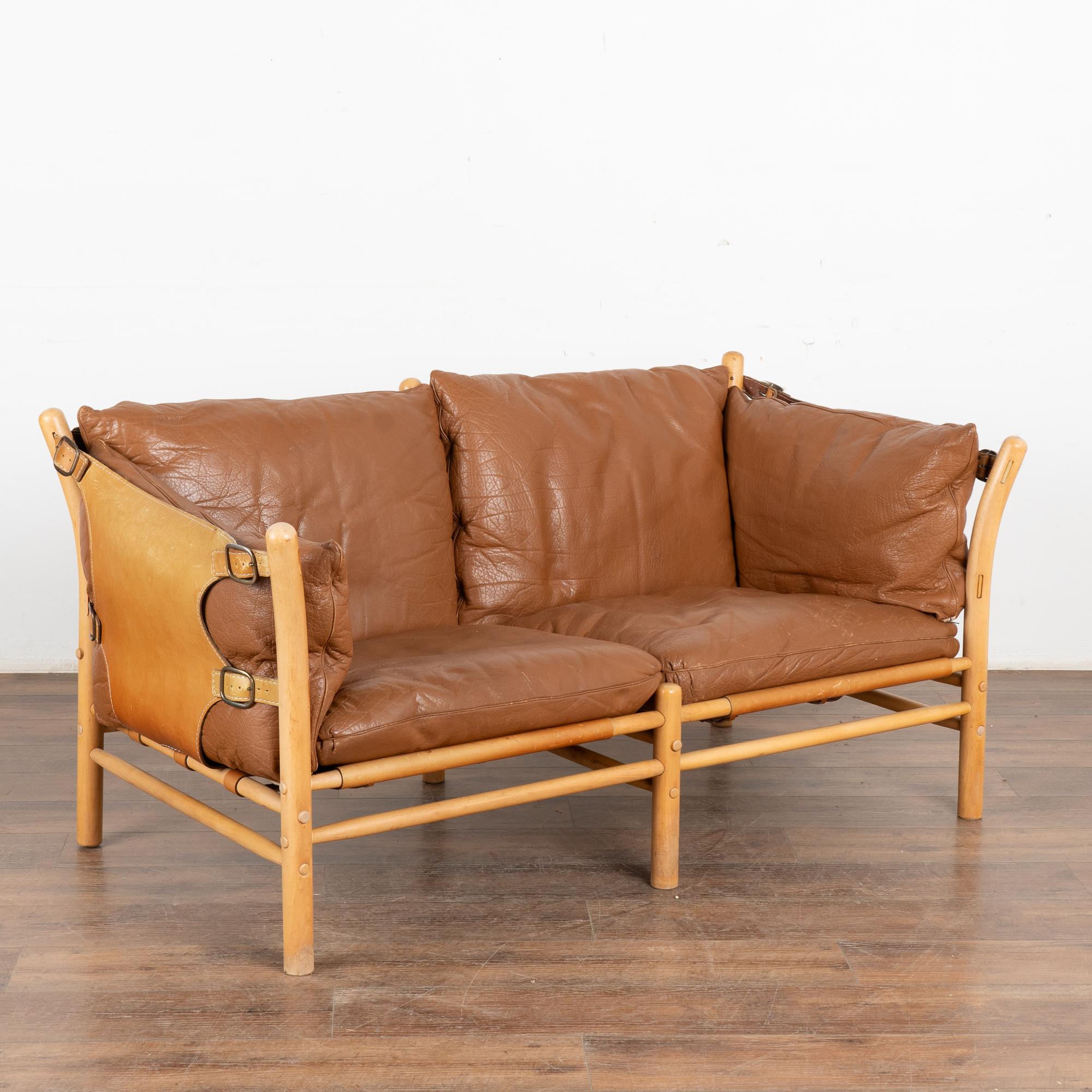 Mid-Century Modern two-person sofa designed by Arne Norell. Leather sling sides and back, brass hardware, loose cushions with zippered covers. The Ilona model was inspired by safari furniture and manufactured by Aneby Møbler (makers mark
