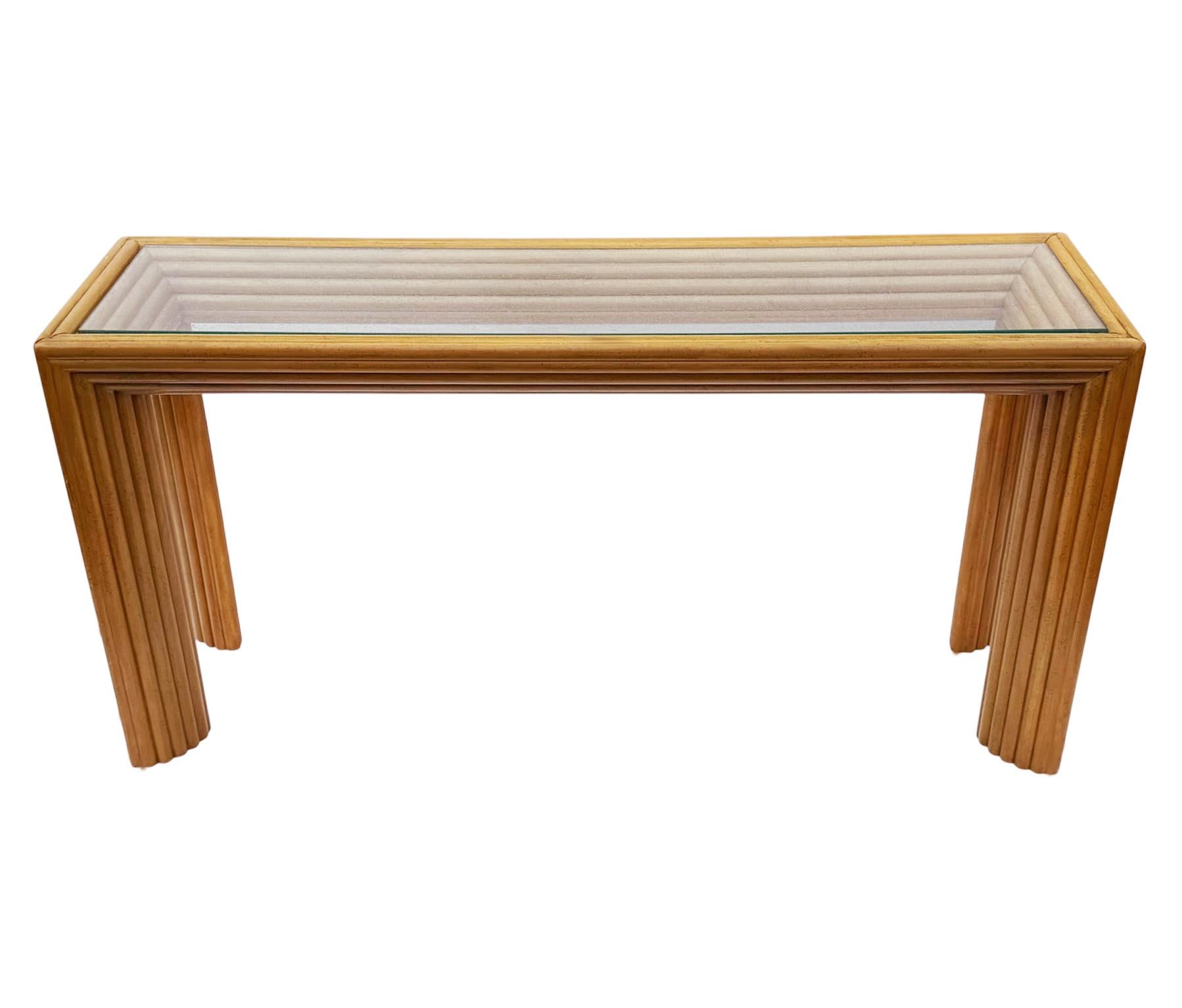 A gorgeous rattan bamboo console table from the 1970's. It features a well built stunning art deco form with clear glass inlayed top. 