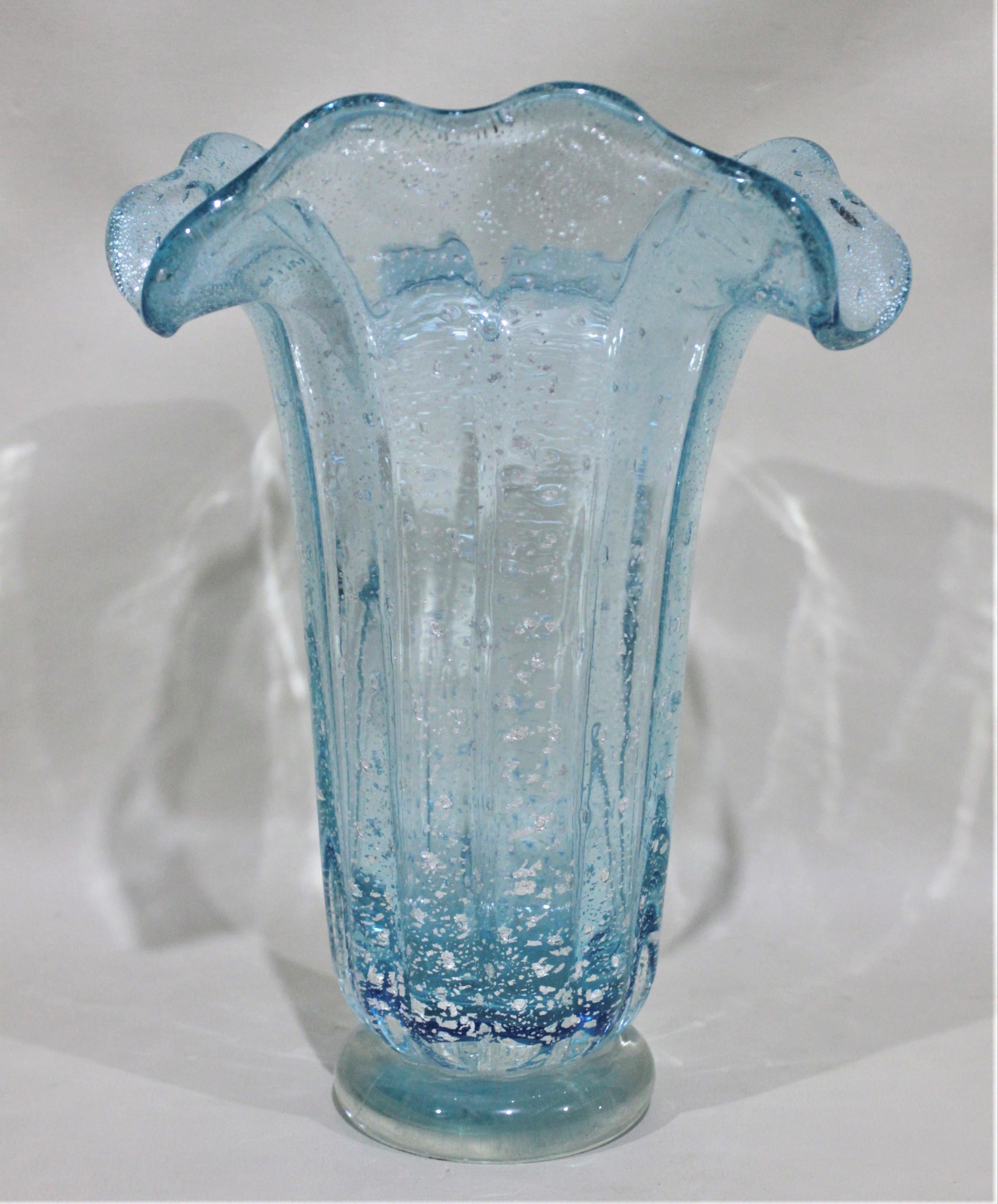 This Mid-Century Modern art glass vase has no markings, but it believed to have been made in Murano Italy and is consistent with the work of Barovier. This thick aqua blue vase has a round base and fluted top and is infused with silver flecks