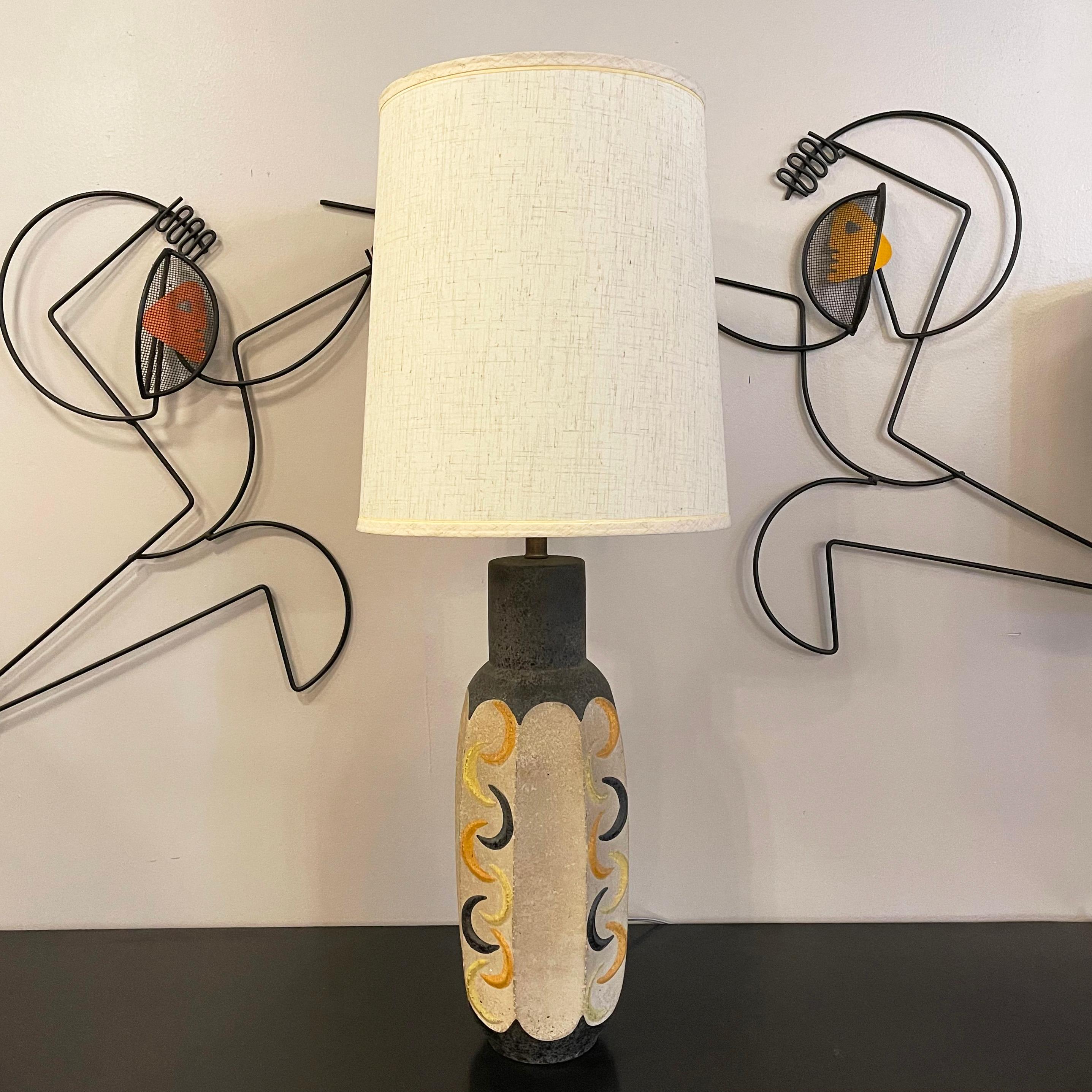 Mid century modern, studio art pottery table lamp by Tye Of California features a faceted body with yellow, orange and gray crescent shapes against a cream background. The height of the ceramic body is 20 inches and the height top of the socket is