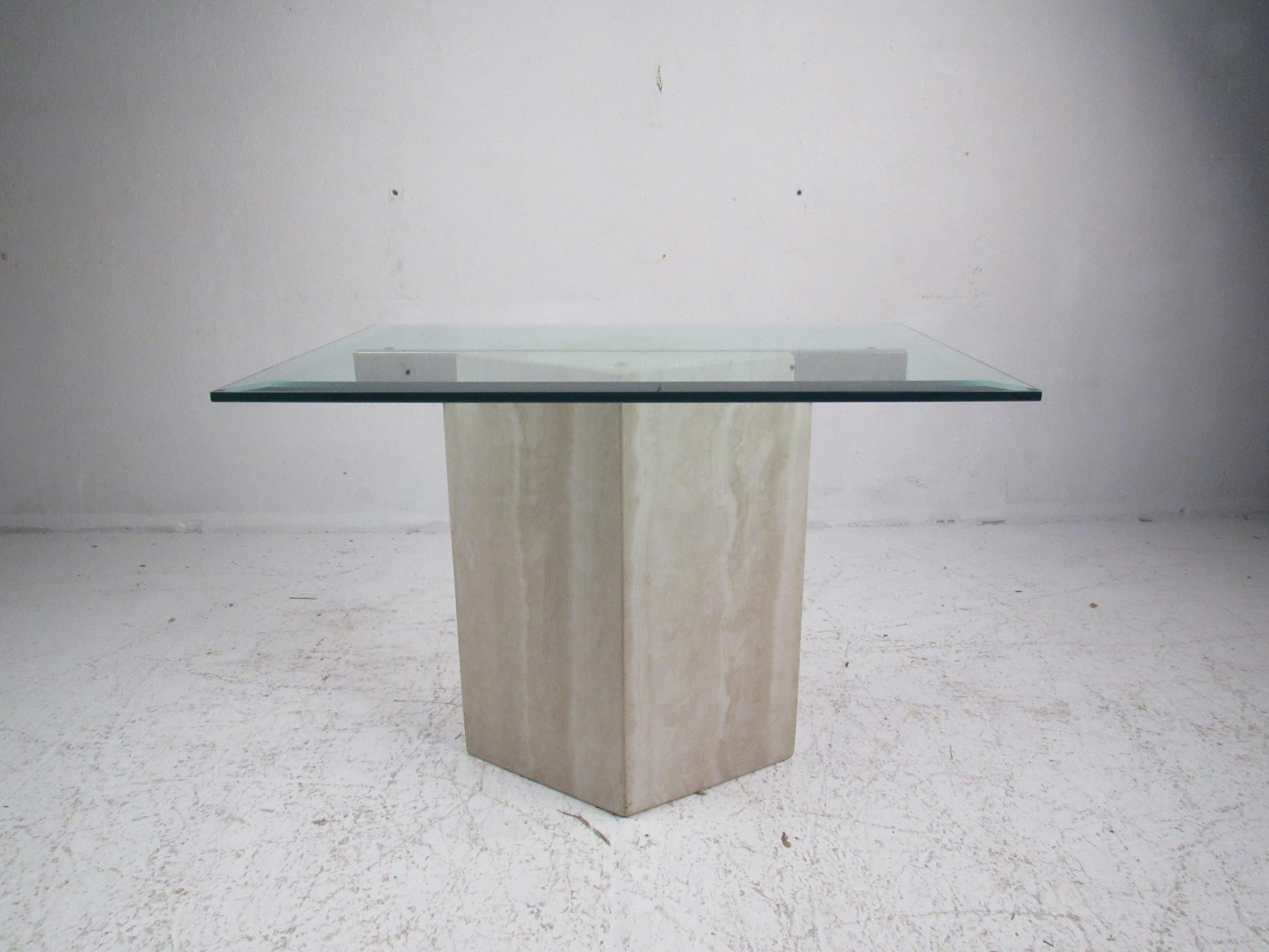 This lovely vintage modern side table features an unusually shaped marble base with a brass support resting in the center. A lightly tinted green rectangular glass top with beveled edges sits comfortably on top. The heavy diamond shaped beige marble