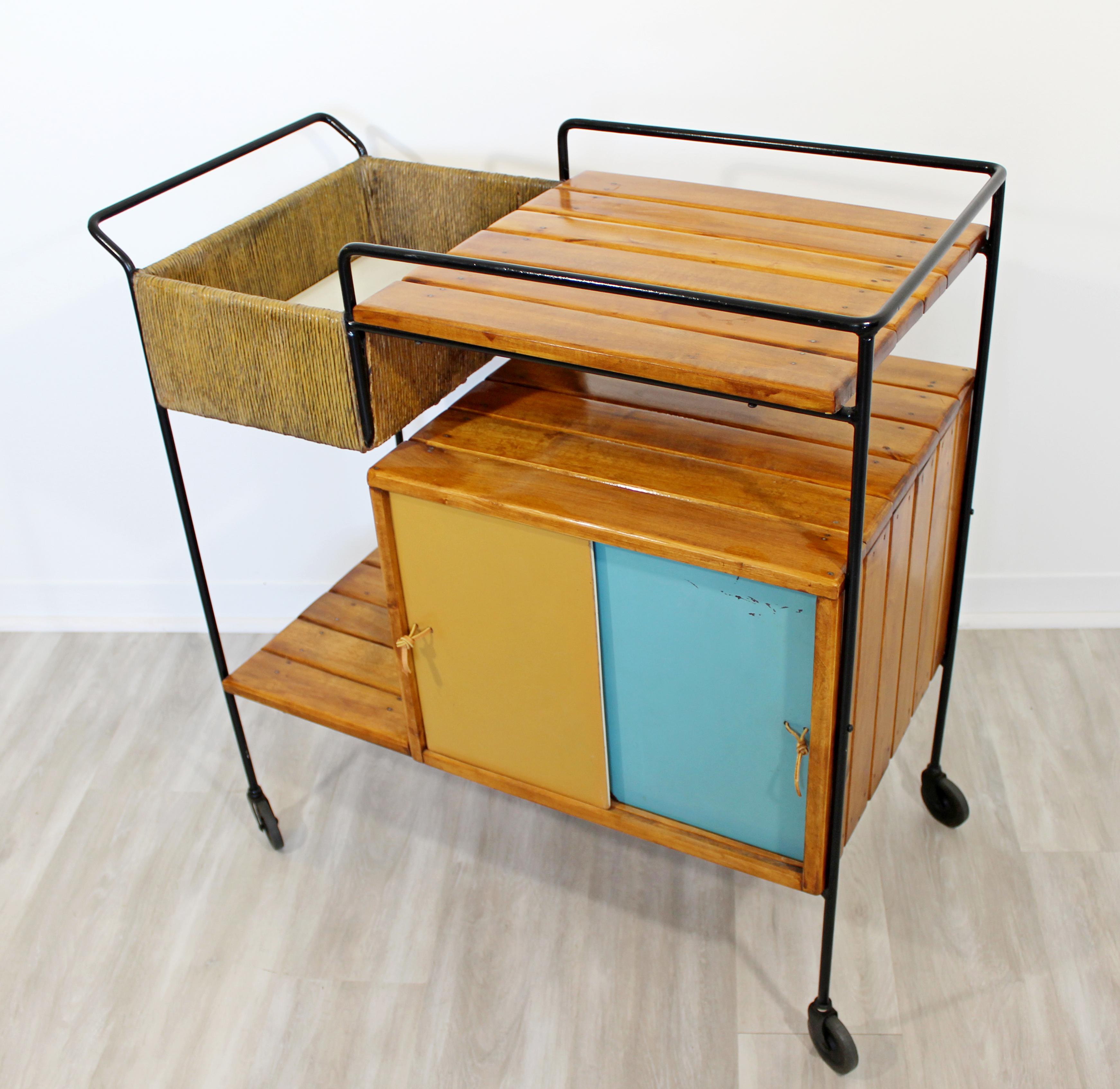 For your consideration is a charming, rolling bar or serving cart, made of wrought iron, with wooden slat shelves, a rush cubby, and four blue and beige sliding doors, by Arthur Umanoff, circa the 1950s. In very good vintage condition. The