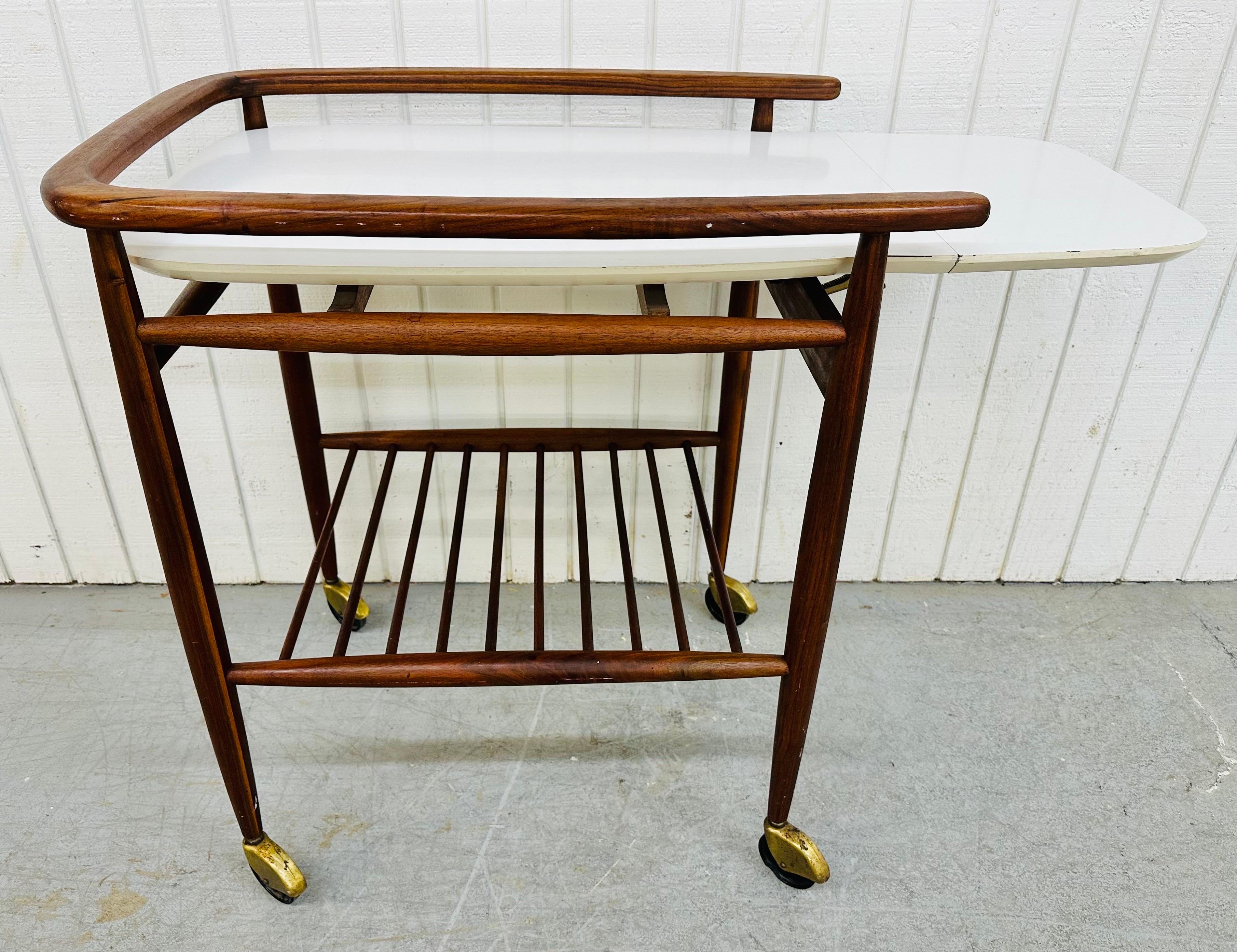 This listing is for a Mid-Century Modern Walnut Bar Cart. Featuring a white laminated serving top, a walnut frame with bottom shelf, and original wheels. This is an exceptional combination of quality and design by Arthur Umanoff!