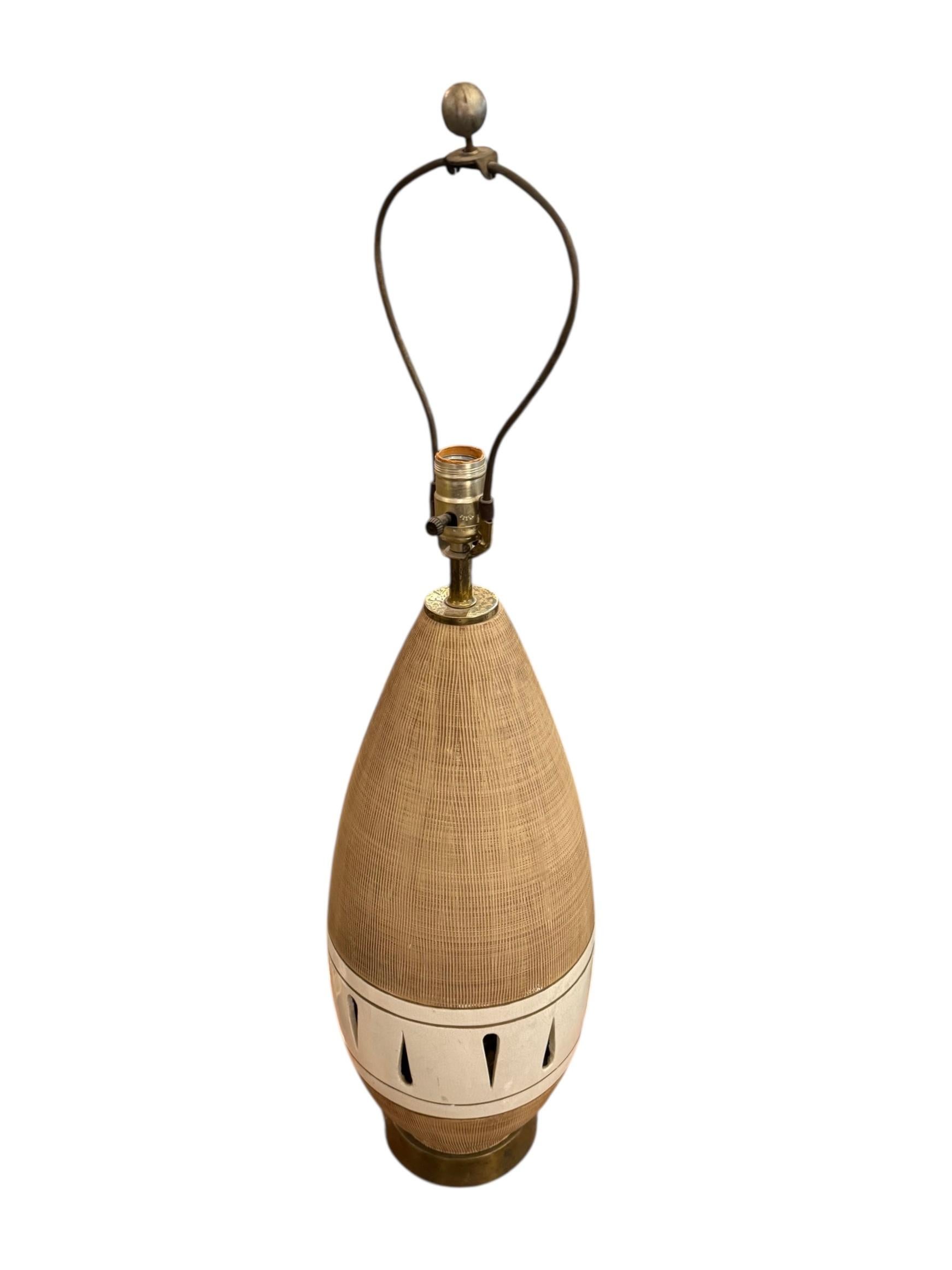 Celebrate the golden age of American design with this stunning Mid-Century Modern Atomic Age Ceramic Table Lamp. Towering with elegance, the teardrop-shaped body features a textured tan glaze with a sculptural white band accented by bold black