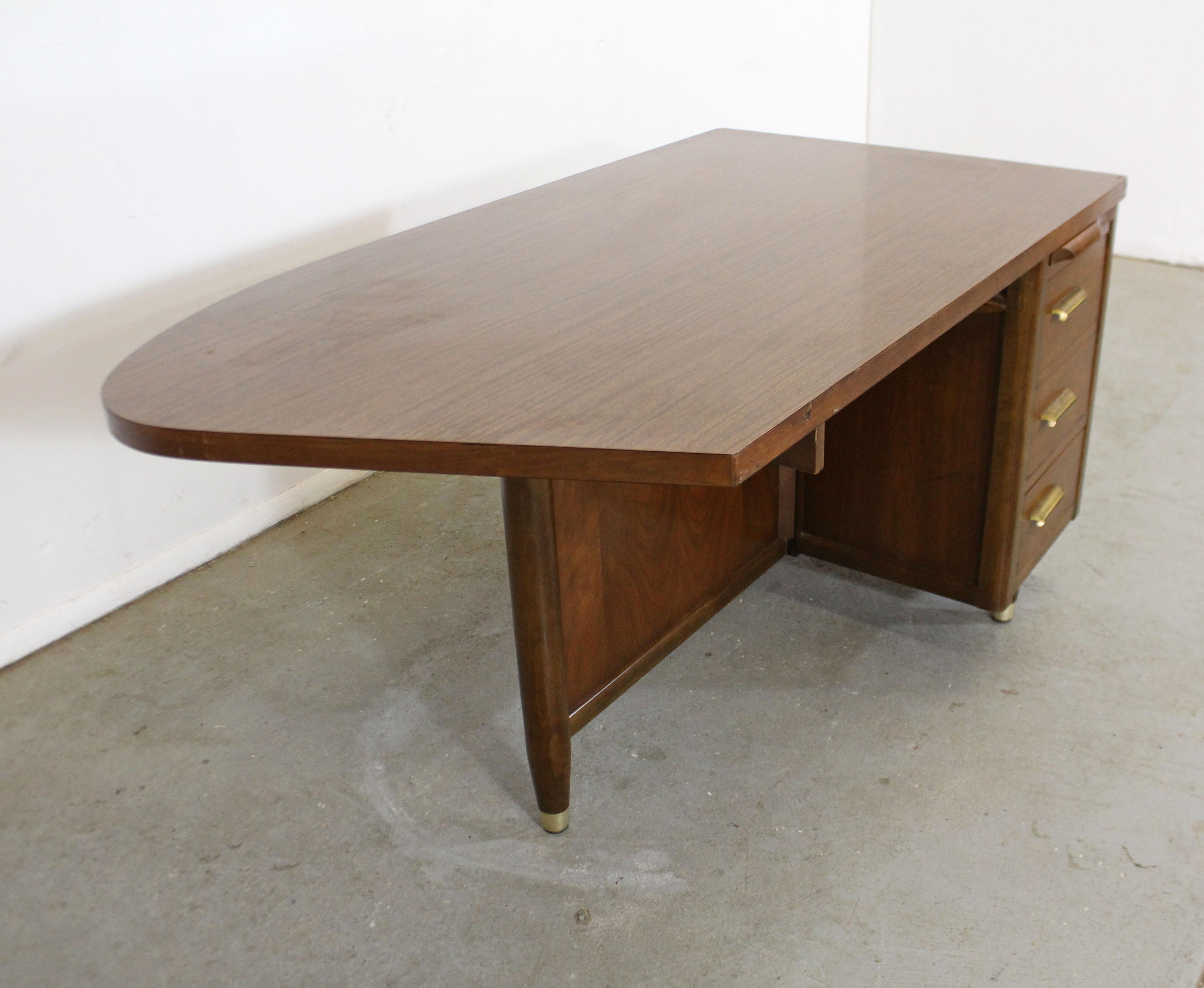 Offered is a vintage Mid-Century Modern desk with a unique shape and ample storage space. Features a curved laminate top and asymmetrical walnut base. One side of the desk features two drawers (one double drawer) and a pull-out surface. The desk is