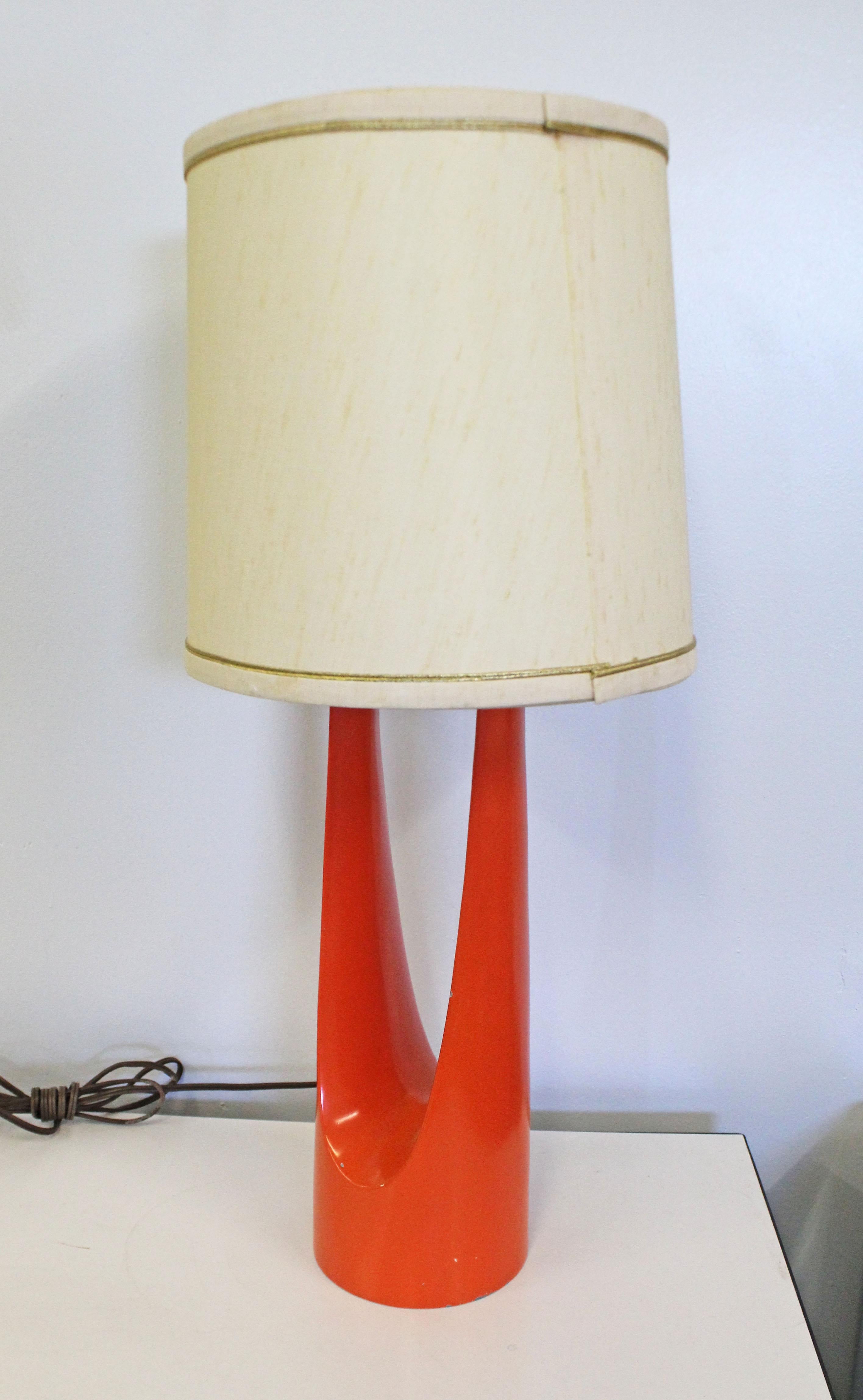 Offered is a vintage Mid-Century Modern table lamp with a unique enameled orange metal base. This piece is in good condition with normal age wear (small chips, scratches, age wear). The lighting works, has been tested. Missing a bottom