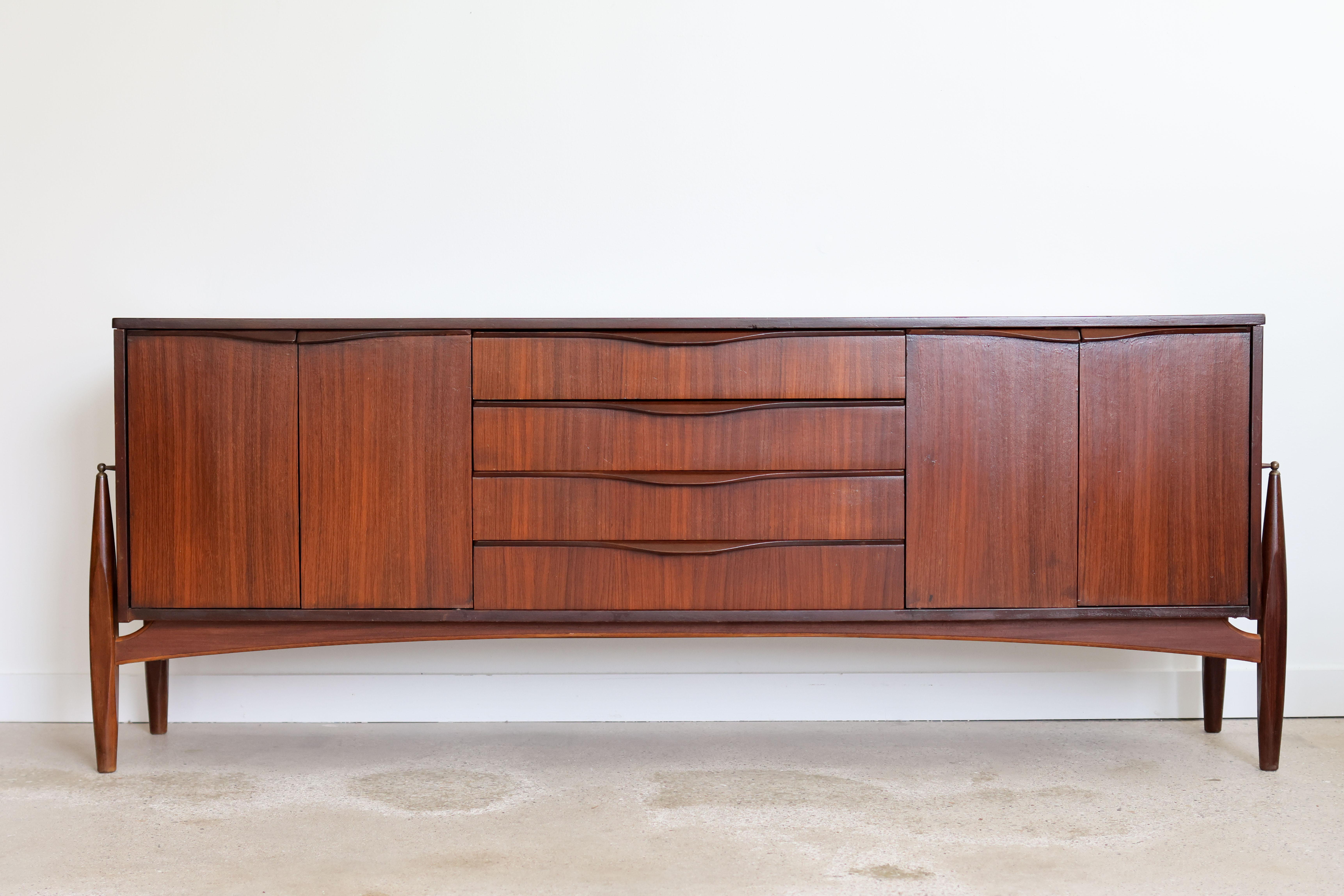 Mid-Century Modern mahogany credenza by Elliotts of Newbury, UK.
Floating legs with little brass accents.
Symmetrical sideboard with two sets of double cabinets and adjustable shelves.
Four dovetailed drawers.
Excellent vintage condition.

77 1/2”