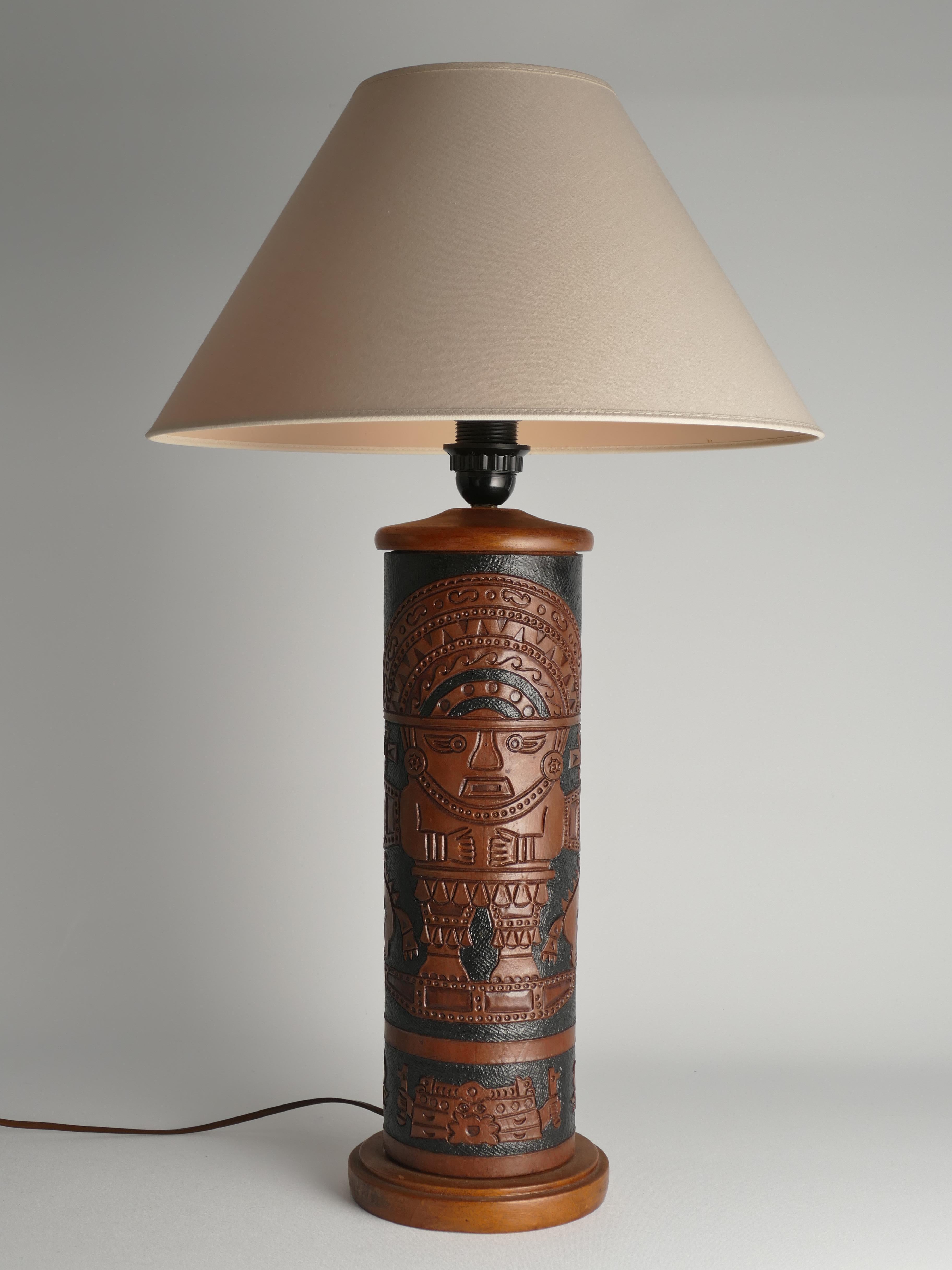 This table lamp showcases what appears to be a hand-tooled leather base with black and brown Aztec mural design. The lamp's base, both at the bottom and top, appears to be crafted from walnut.

DIMENSIONS
Height (fixture not included): 38 cm.