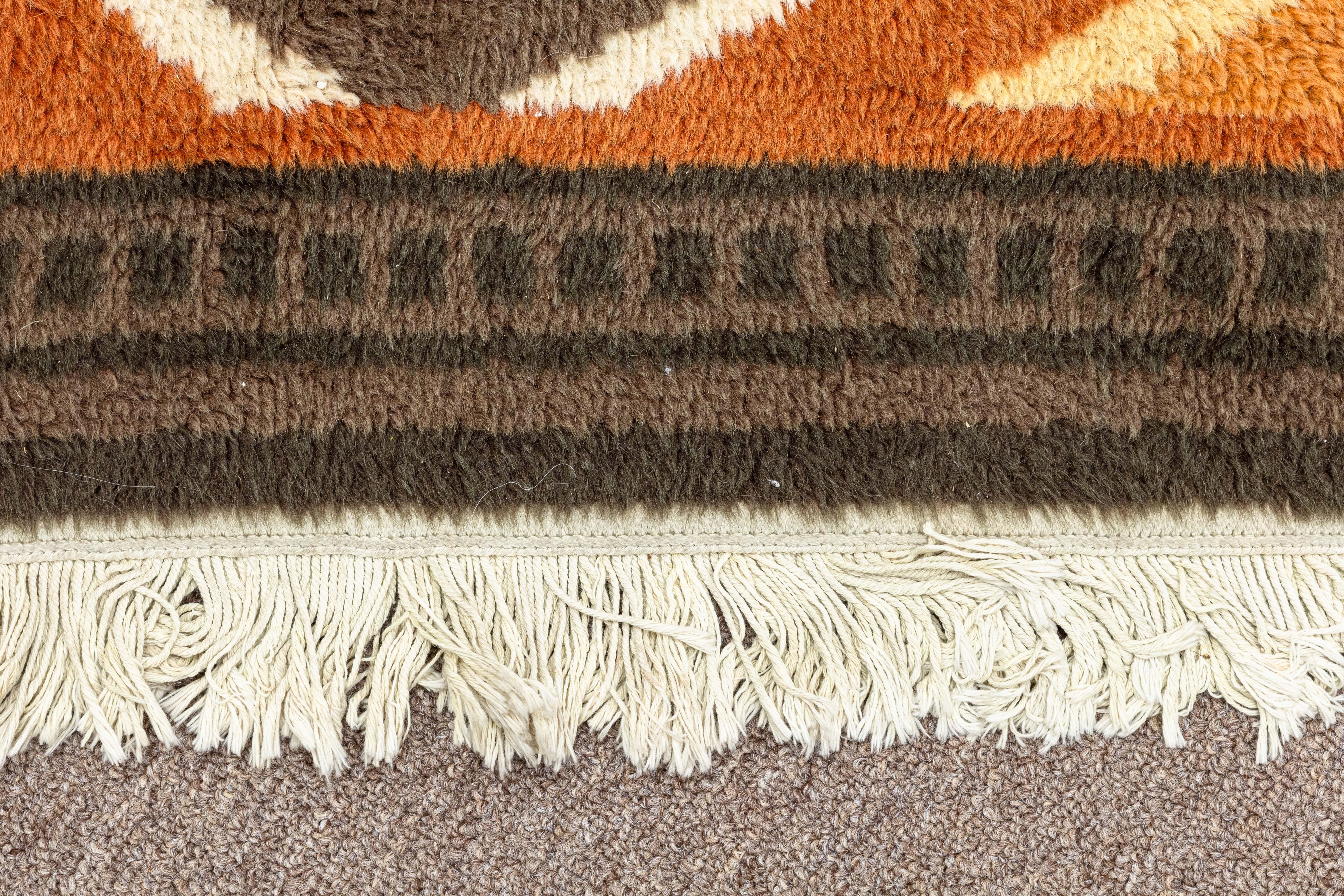 A mid century modern Aztec brown and orange area rug. This is a gorgeous area rug with a fantastic design. This piece features a mix of browns and oranges and depicts a series of animals and geometric patterns. The color palette and patterning makes