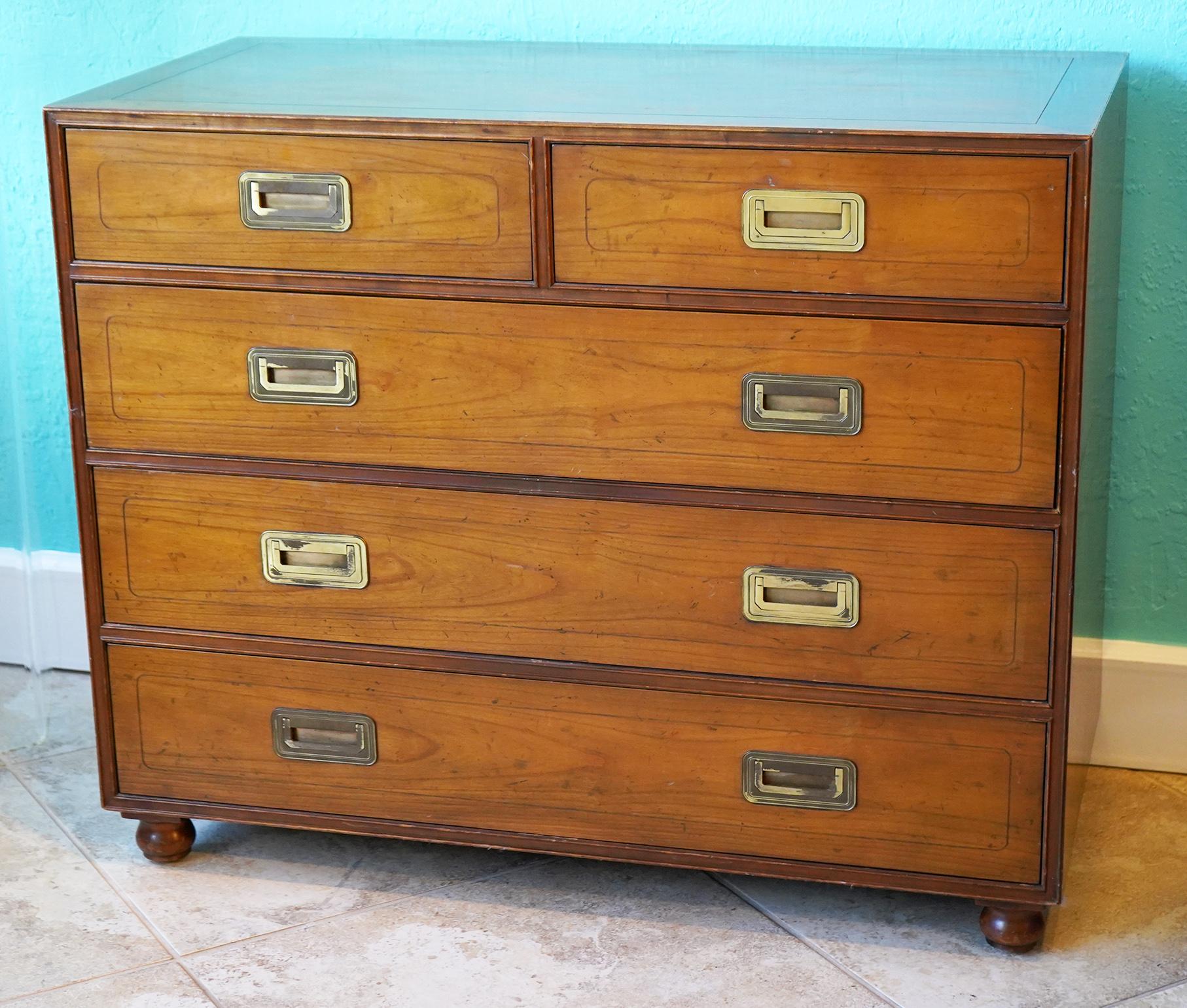 This mid century Baker campaign style two over three drawer walnut chest featured a banded top above five dovetailed drawers with solid brass campaign style pulls resting on turned feet.