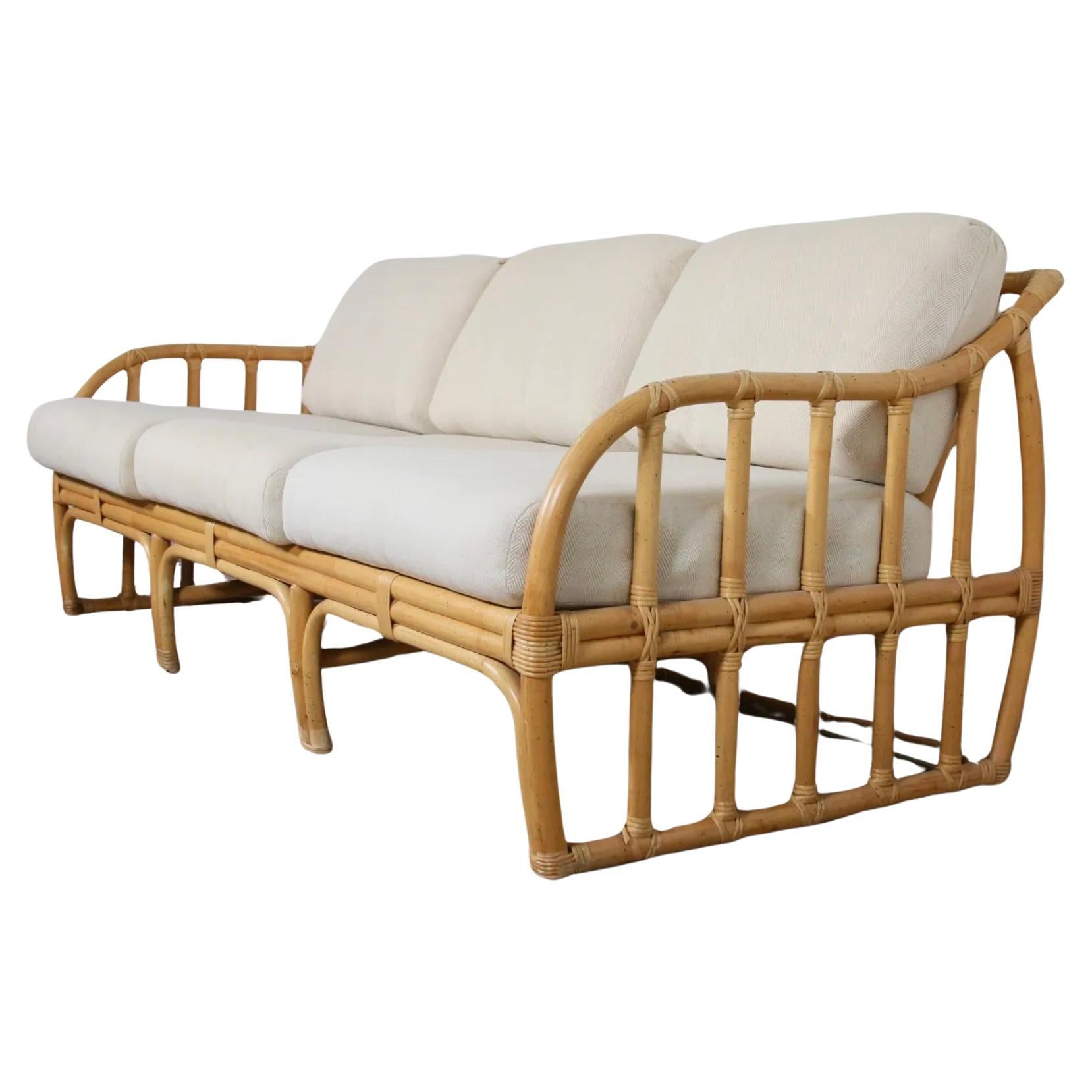 Mid Century Modern bamboo and rattan sofa by Ficks Reed. Cincinnati, OH, 1970s. Bentwood bamboo and rattan frame in sandstone finish with burlap supporting white seat and back cushions. Cushions are in Vintage condition can use as is or reupholster