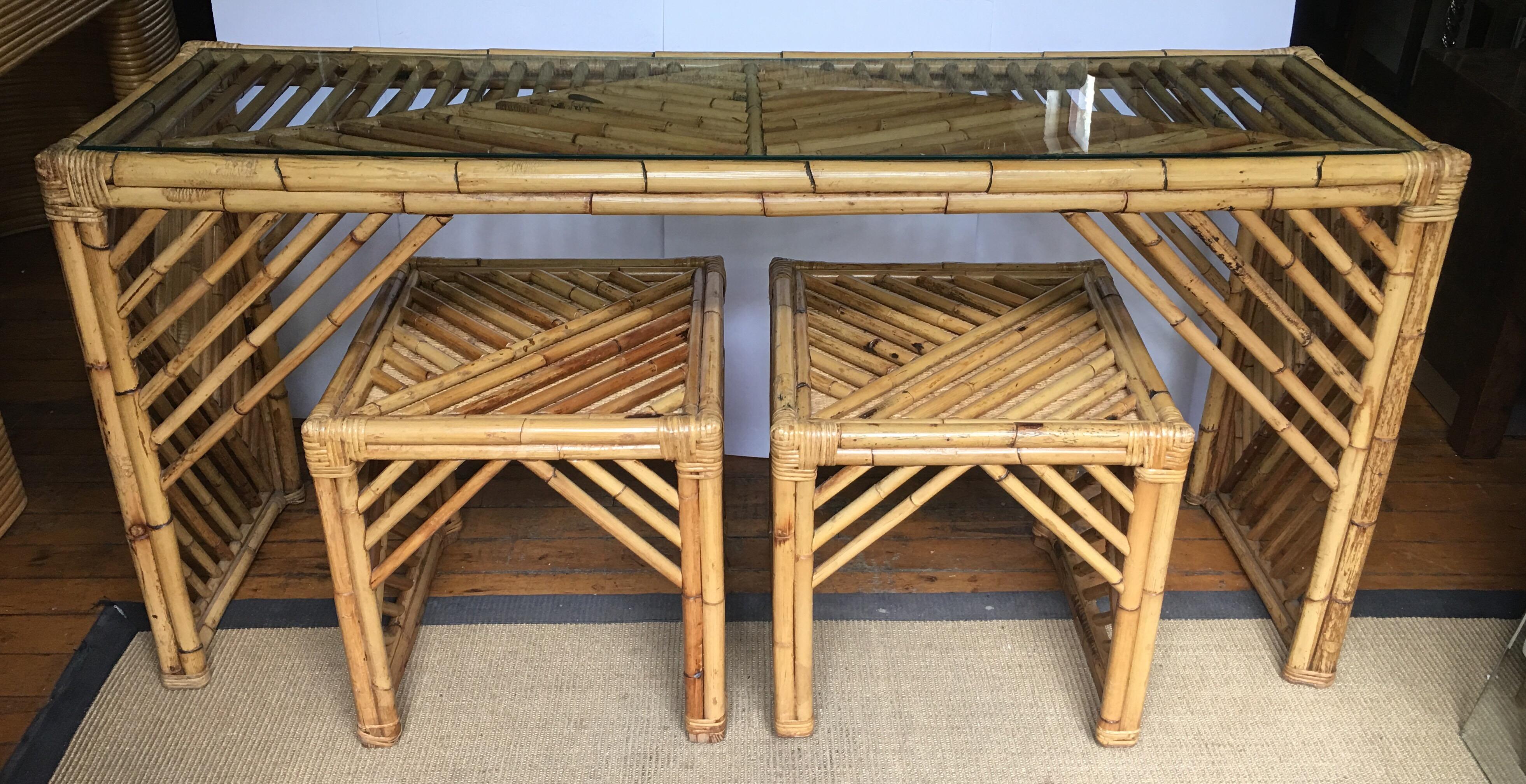 Mid-Century Modern bamboo console sofa table with matching pair of ottoman stools. This Hollywood Palm Regency style table features a graphic geometric design in a traditional fretwork pattern. Clear glass top is removable. Coordinating pair of