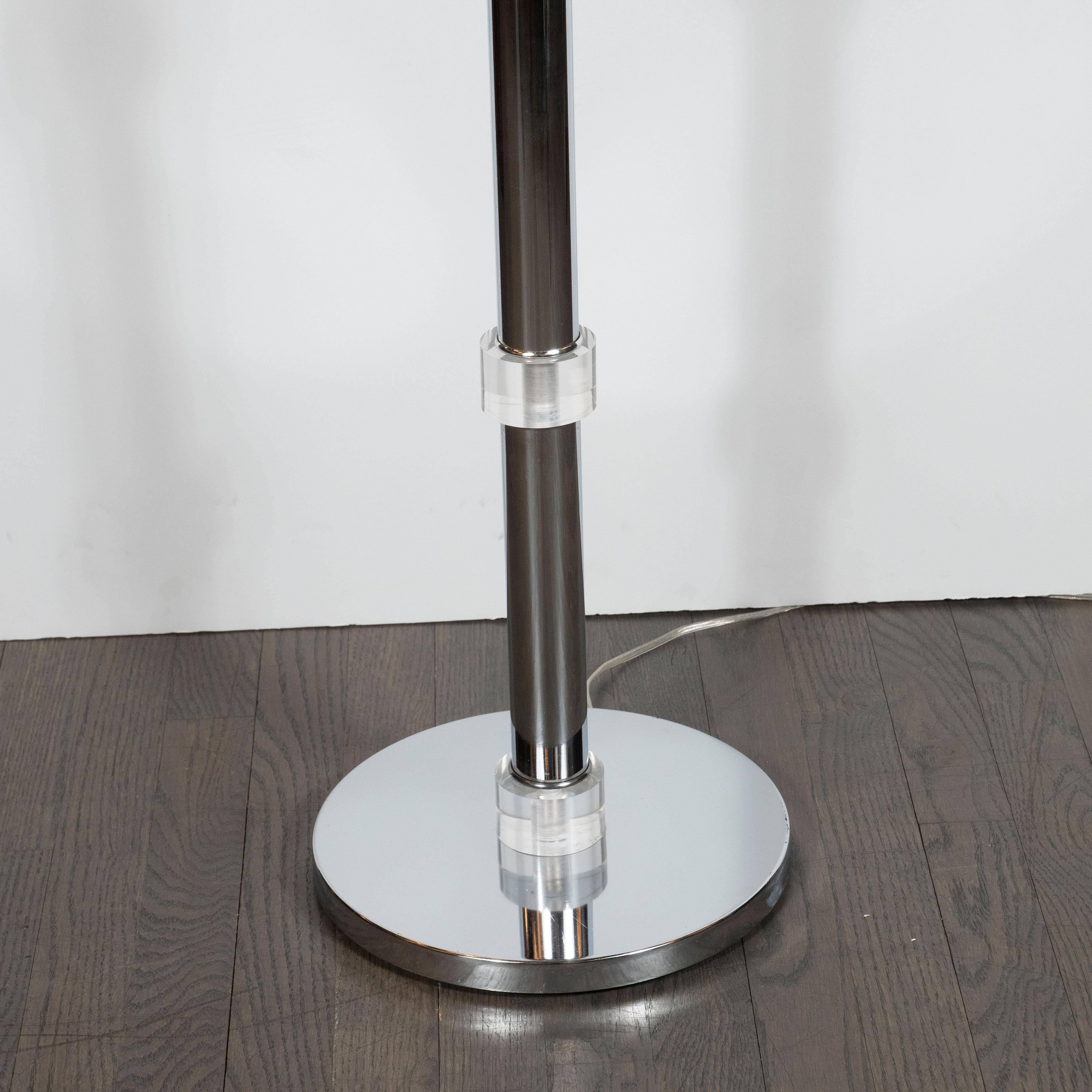 This refined floor lamp was realized in the United States, circa 1970. It features a cylindrical polished chrome body banded in four places with Lucite embellishments in the same shape. The lamp rests on a circular chrome base, and comes fitted with