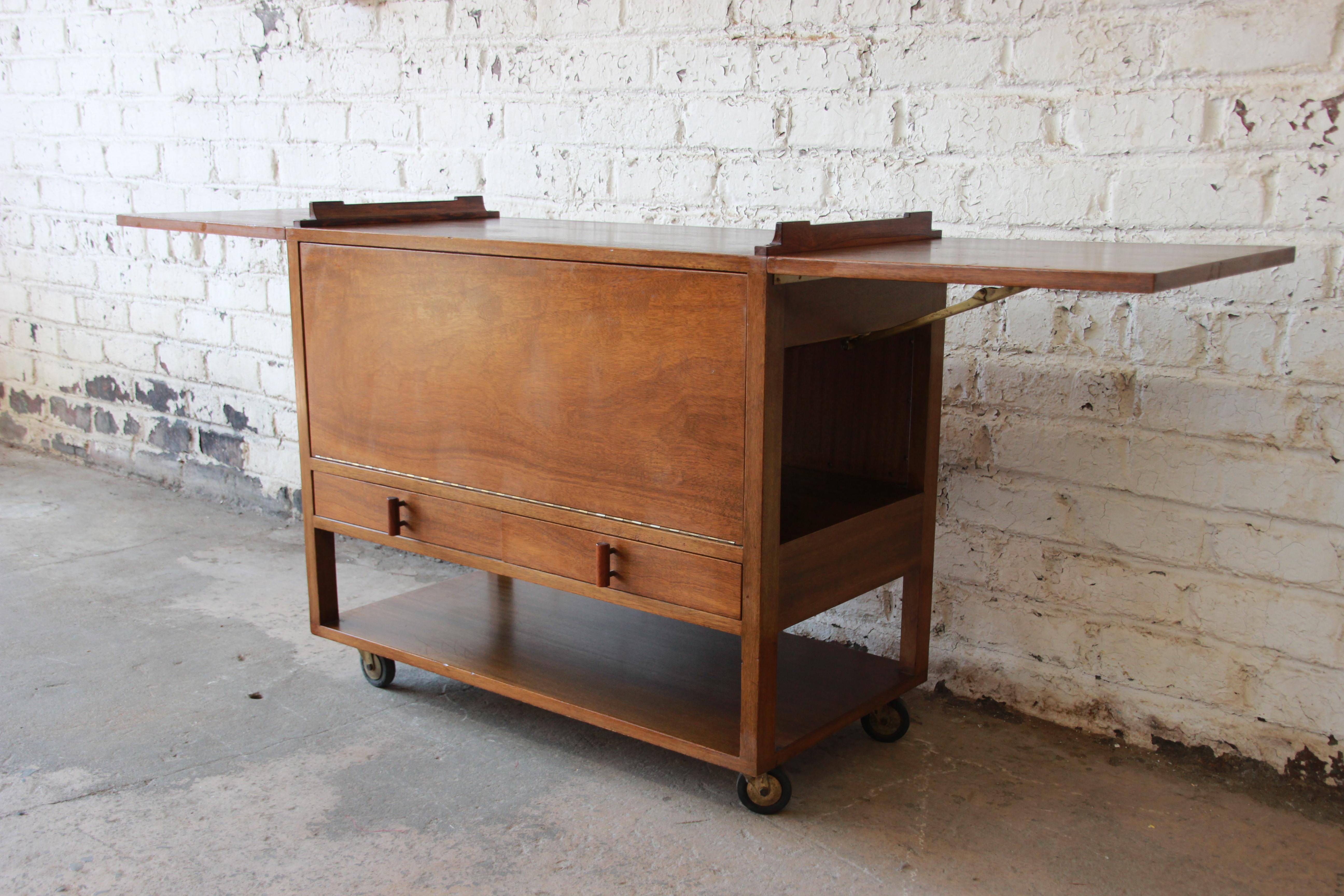 Offering a very nice Mid-Century Modern rolling bar cart by Wormley for Dunbar. The bar features a nicely woven back, two-drawer for storage, a drop-front door that turns into a shelf, and two large leaves. The cart provides lots of room for storage