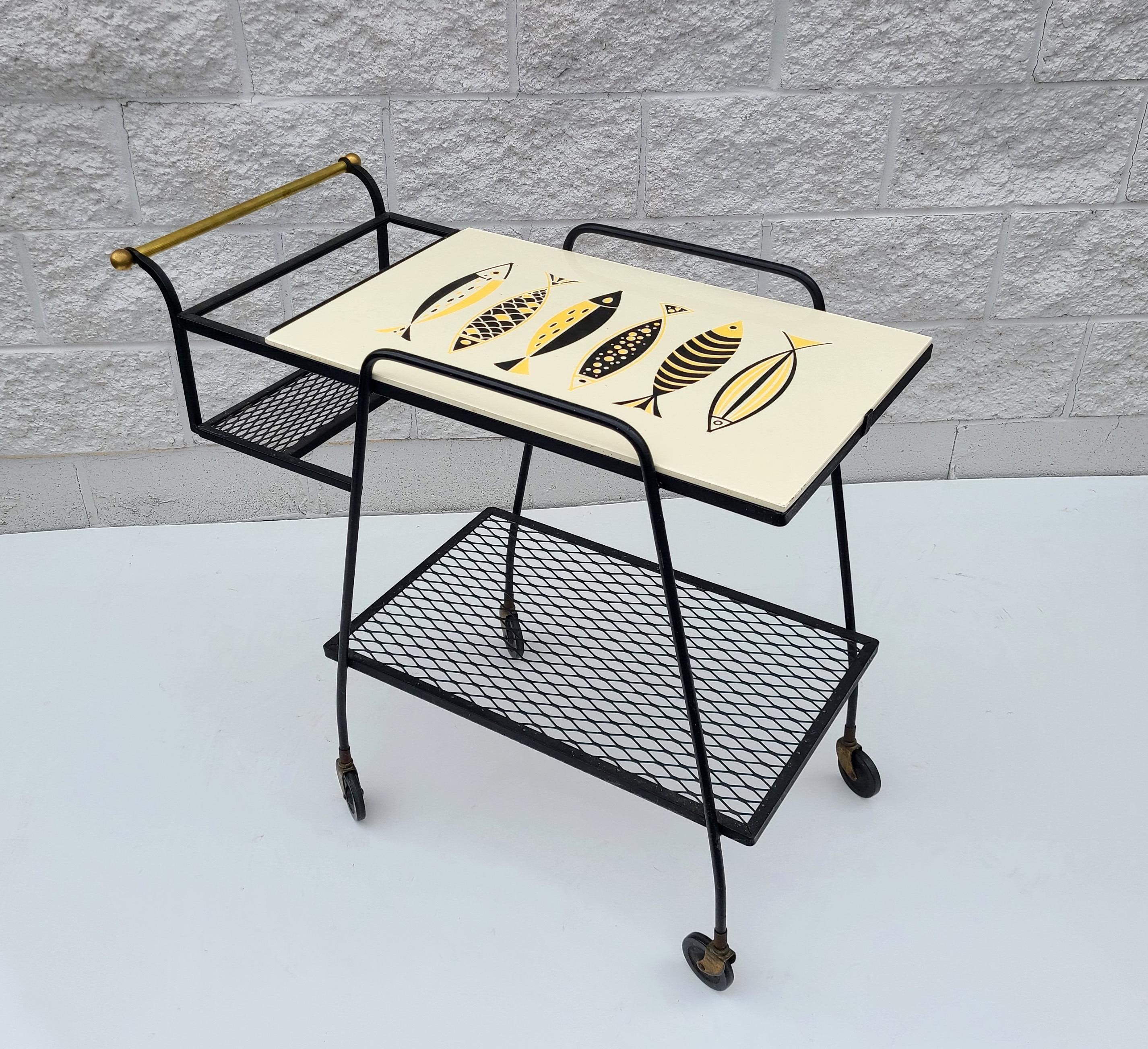 Please message us for a cost effective shipping quote to your location.

Mid-Century Modern bar cart. Wrought iron frame. Brass trim.
Ceramic tile with Fish top Panel.