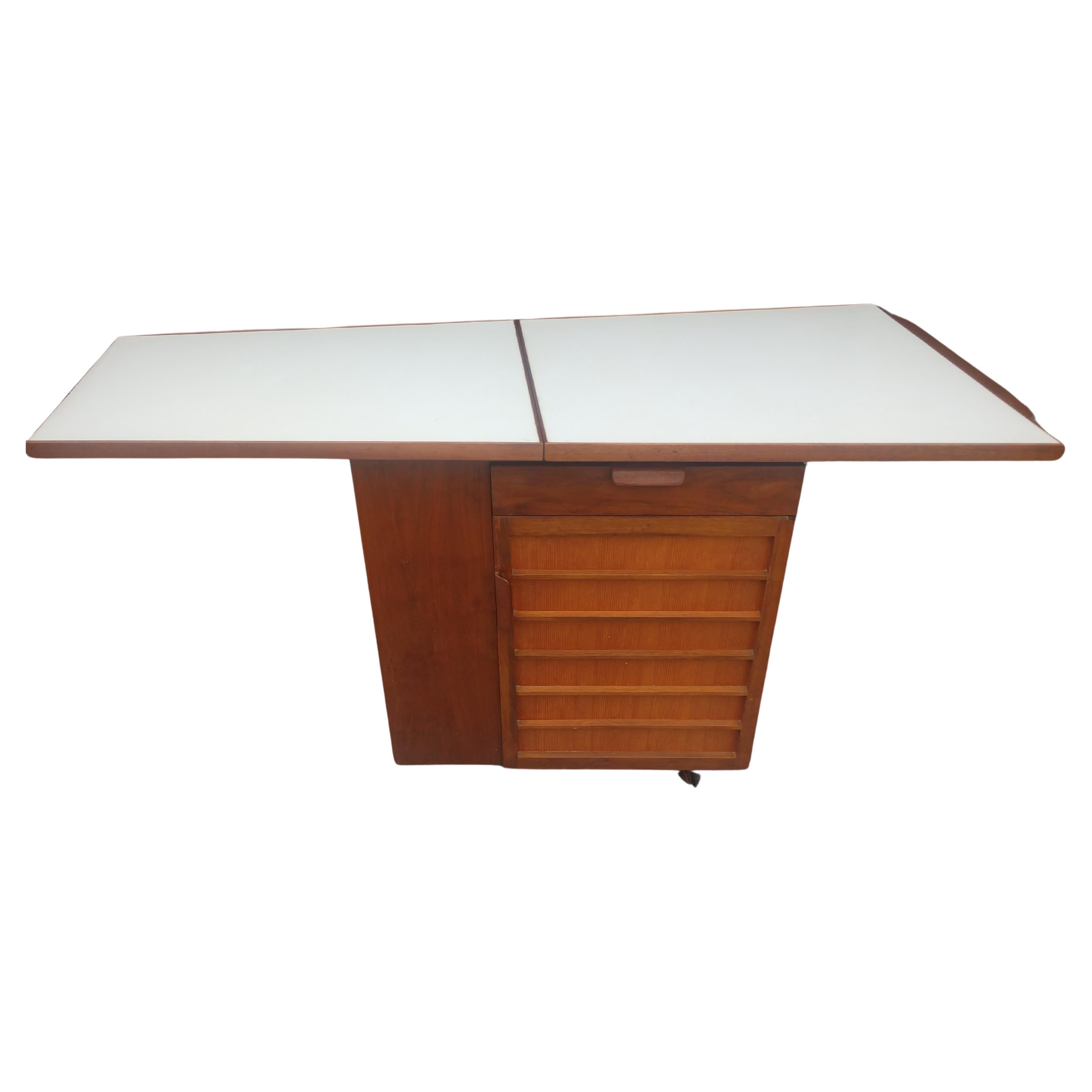 Favoloso carrello/server da bar con piano a ribalta di 27 pollici e 54 quando è sollevato, ripiani per le bottiglie, armadietto per i bicchieri e altre necessità. Il modello n. 5433 è stato creato in noce con una porta d'ingresso a righe in pino.