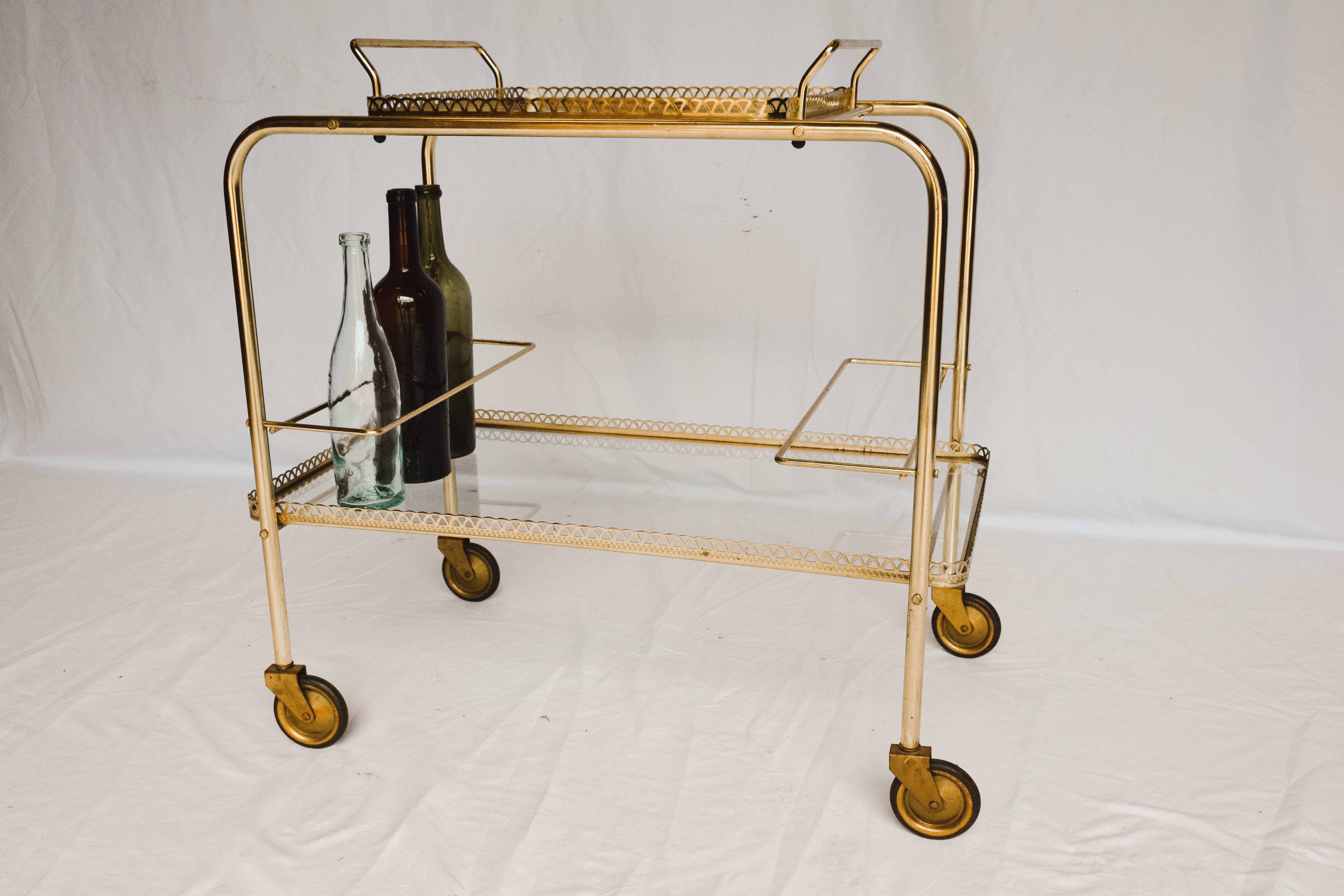 This Mid-Century Modern bar cart is sure to delight. Constructed of brass and glass bringing beauty to the midcentury design. The two glass tiers provides ample space for all your bar needs. The top tray lifts off for additional service. It also has