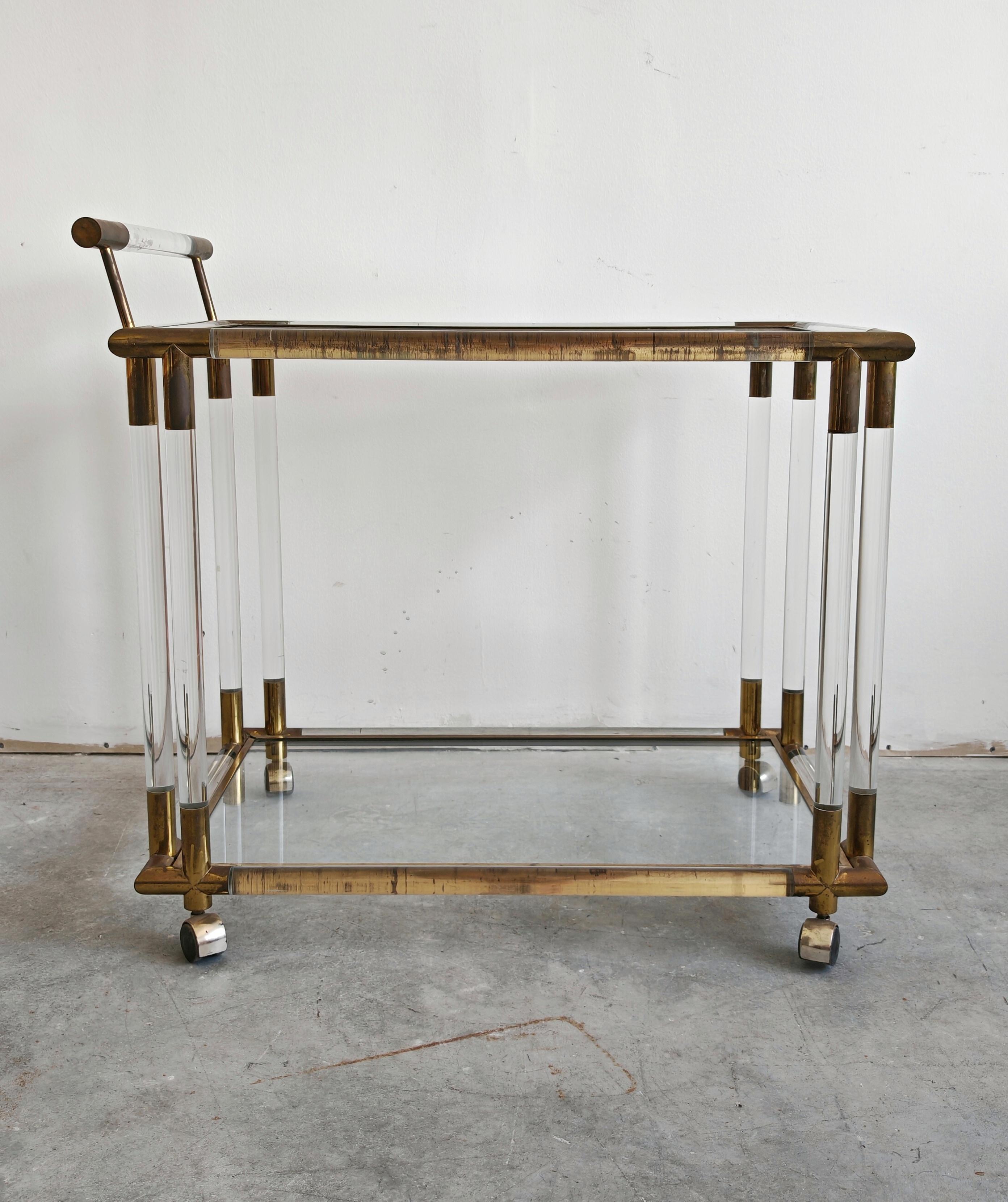 In this listing you will find a luxurious and sleek Mid Century Modern bar cart in lucite, bronze and glass. The bar cart has two tiers withe tops made of glass, while it's overall structure is done in lucite, with bronze details. This very elegant