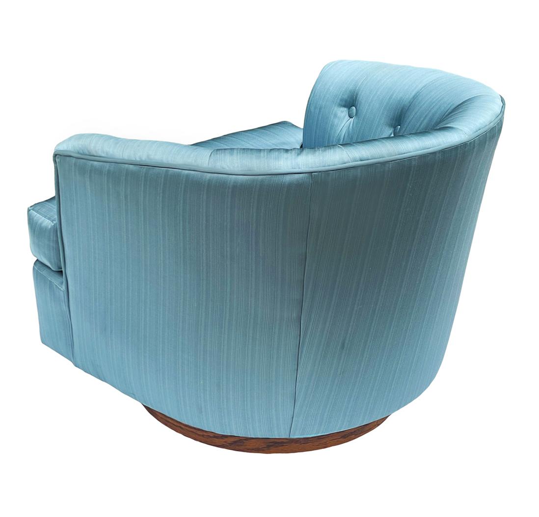 A super comfy matching pair of barrel back lounge chairs circa 1960's. These feature swiveling walnut base with blue fabric. Fabric is old and should be replaced.