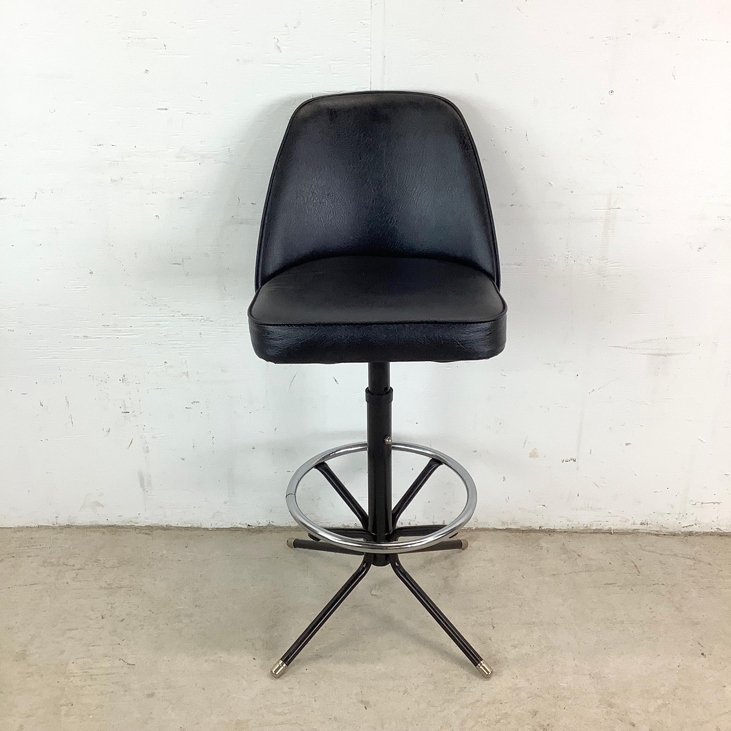 Questo sgabello girevole vintage incarna l'ingegno minimalista del design di metà secolo. La seduta sagomata, rivestita in vinile nero, offre un punto di appoggio strutturato ma confortevole, mentre lo schienale compatto offre il sostegno necessario