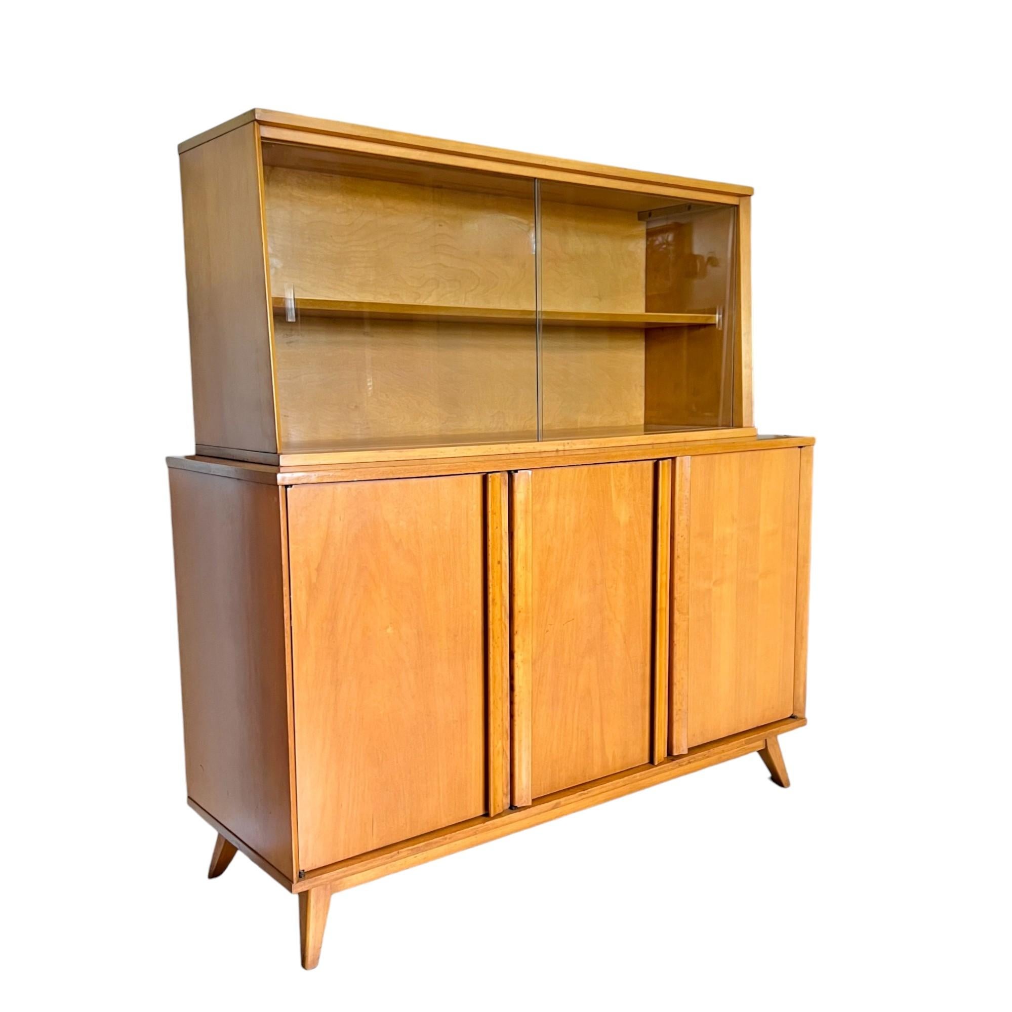 A vintage mid-century modern two piece buffet and hutch by Viko Baumritter circa 1960. Crafted from maple wood with a beautiful natural aged patina, this spectacular display cabinet features a slant front hutch with sliding glass doors and a buffet