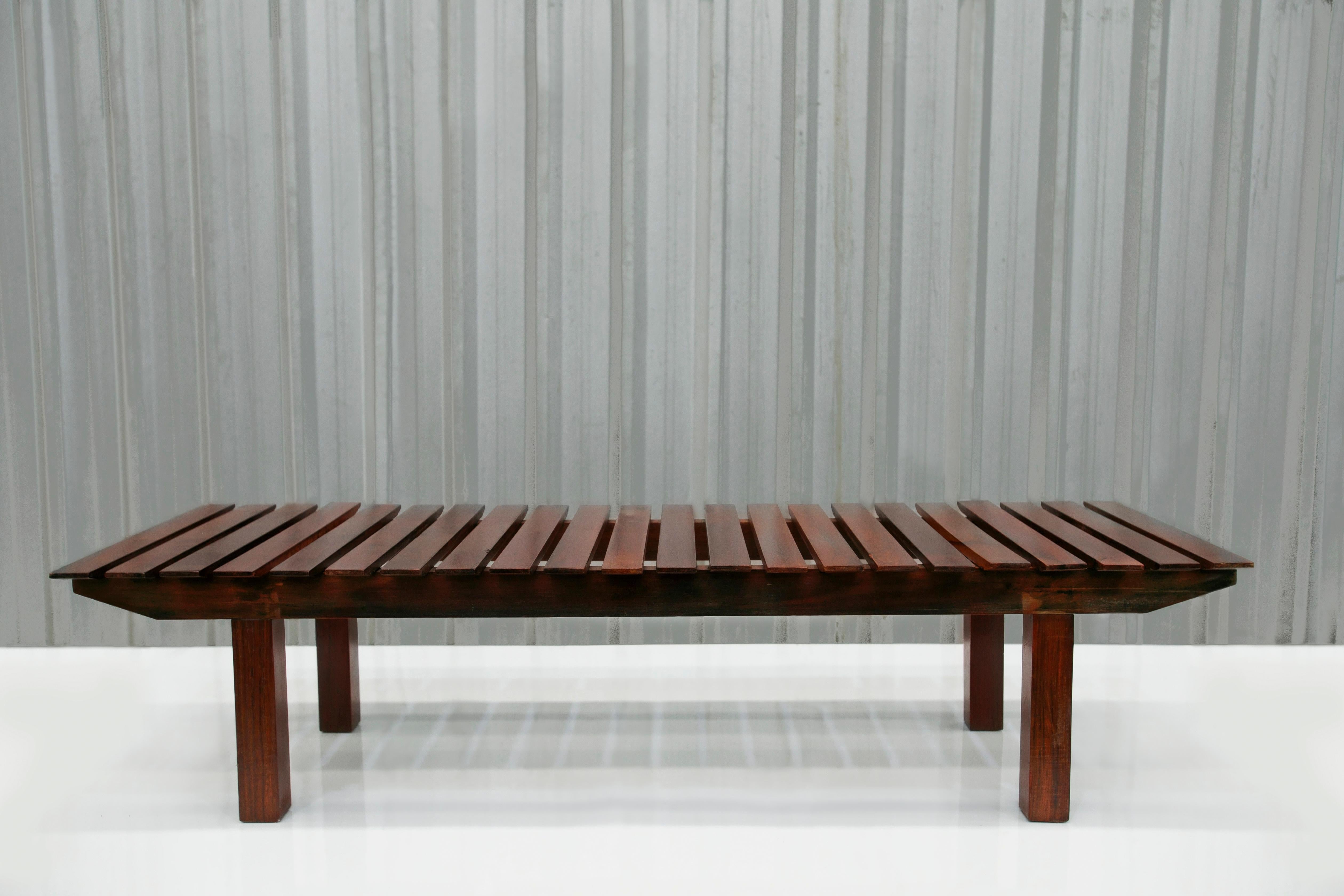 Ce banc est entièrement fabriqué en bois de rose brésilien, également connu sous le nom de jacaranda, réputé pour sa couleur riche et ses veinures distinctives qui rehaussent sa beauté. Les pieds sont formés par quatre pièces de bois verticales qui