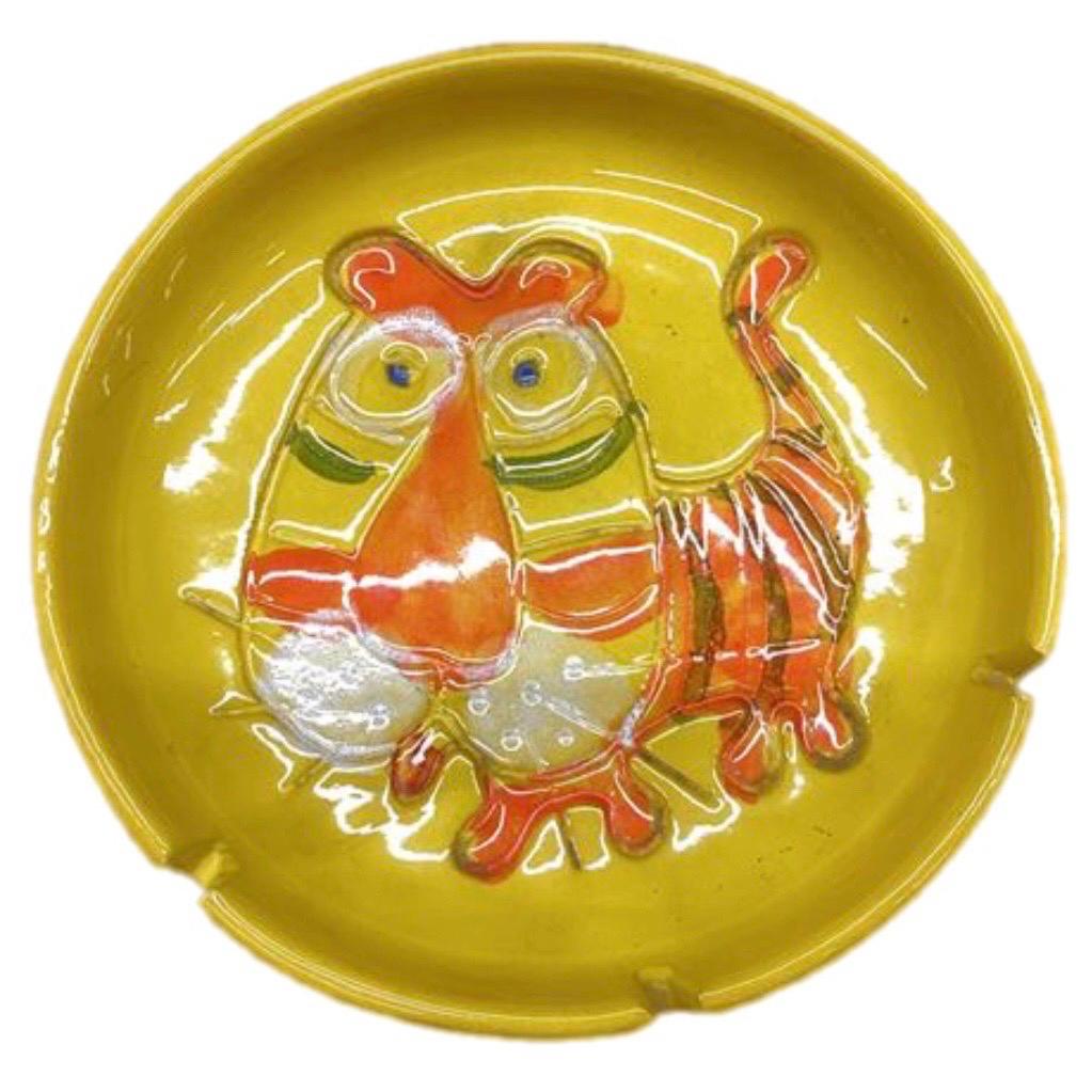 An oversized midcentury Tiger ashtray, signed B. Walsh (Bennett Walsh), dated 1973.  Made of stoneware and showing an incised image of a tiger glazed in primary pop-colors of orange on yellow. The deep rim has three slots for holding cigarettes. A