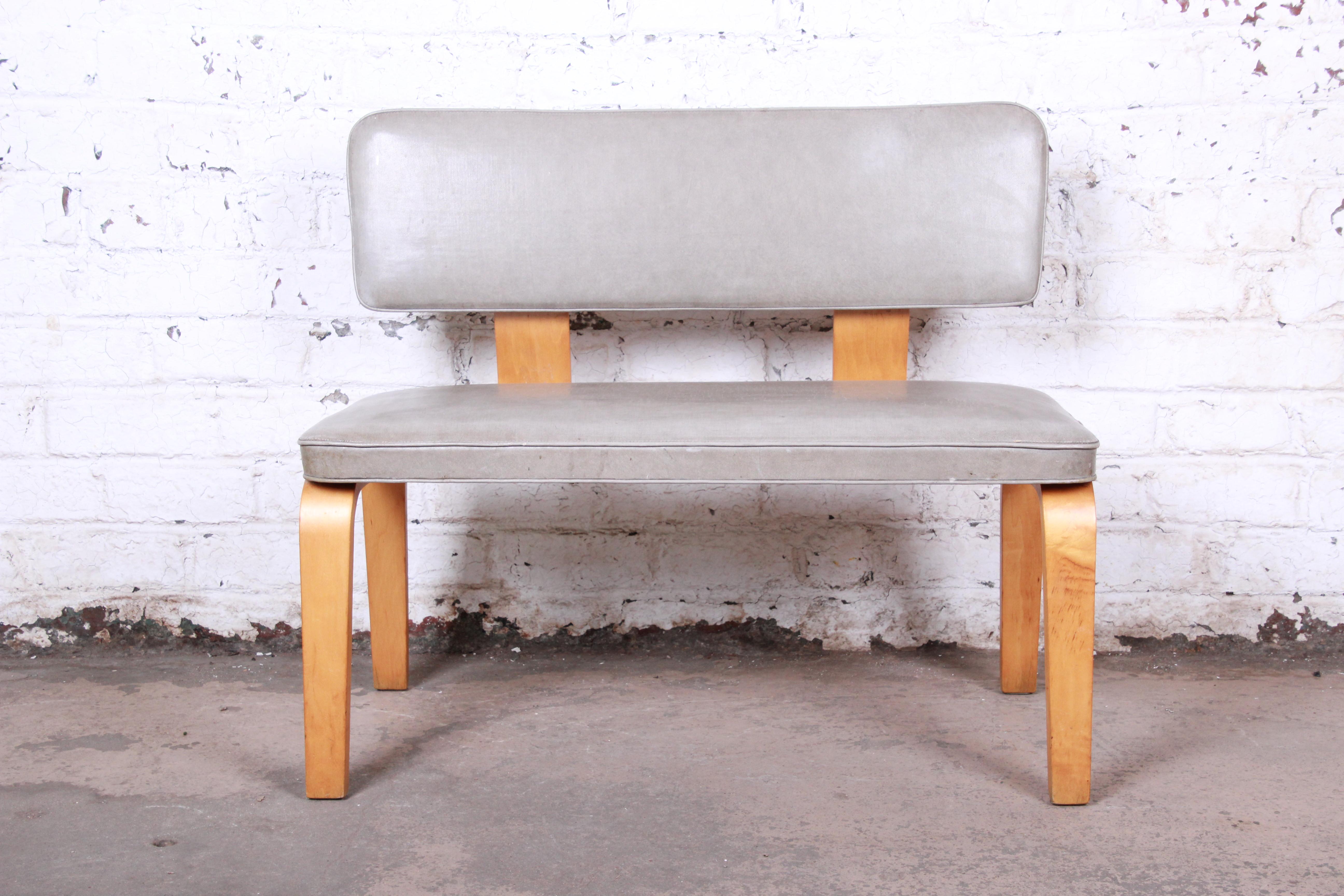 A sleek and stylish Mid-Century Modern bentwood bench attributed to Thonet. The bench features a unique bentwood frame with floating backrest and original gray vinyl upholstery. It is sturdy and in good original vintage condition.

Measures 36.5
