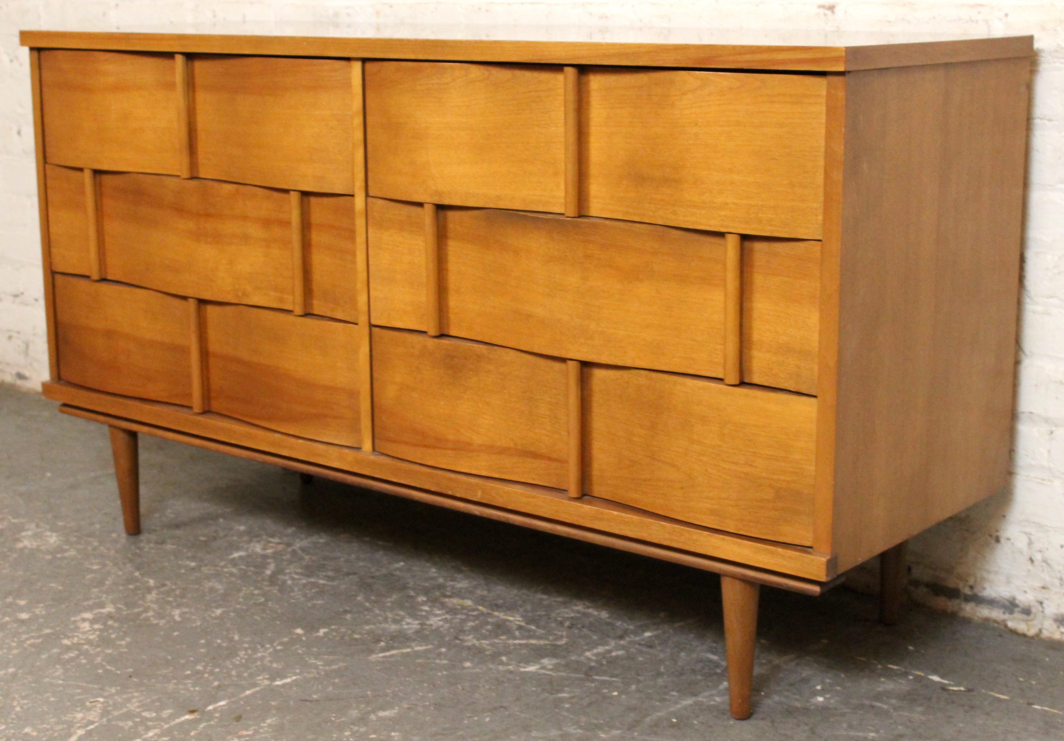 Una icónica cómoda de madera curvada moderna de mediados de siglo diseñada por Johnson Carper. Esta llamativa pieza presenta una escultural fachada de aspecto entretejido con nueve espaciosos cajones y tiradores verticales integrados, mostrando la
