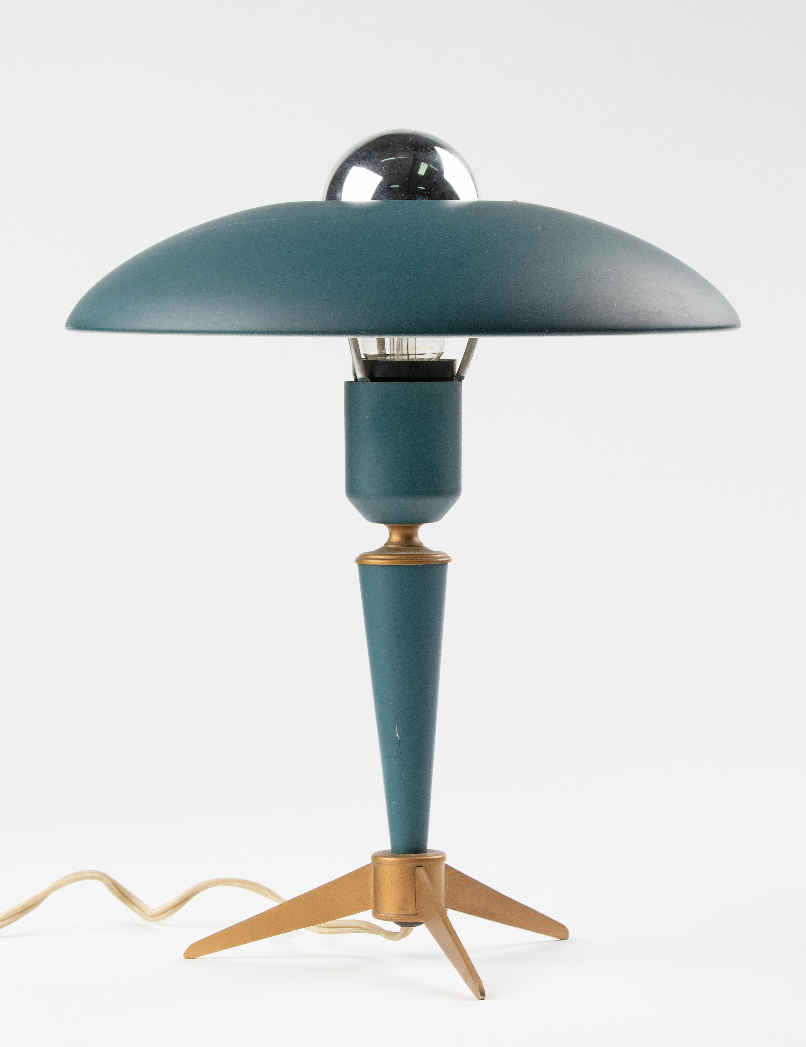 A stylish desk or table lamp on a tripod base. The design is by Louis Kalff for Philips, model is ‘Bijou’. Made of metal and brass. It has the original petrol green finish, which combines beautiful with the gilt color tripod base. with the original