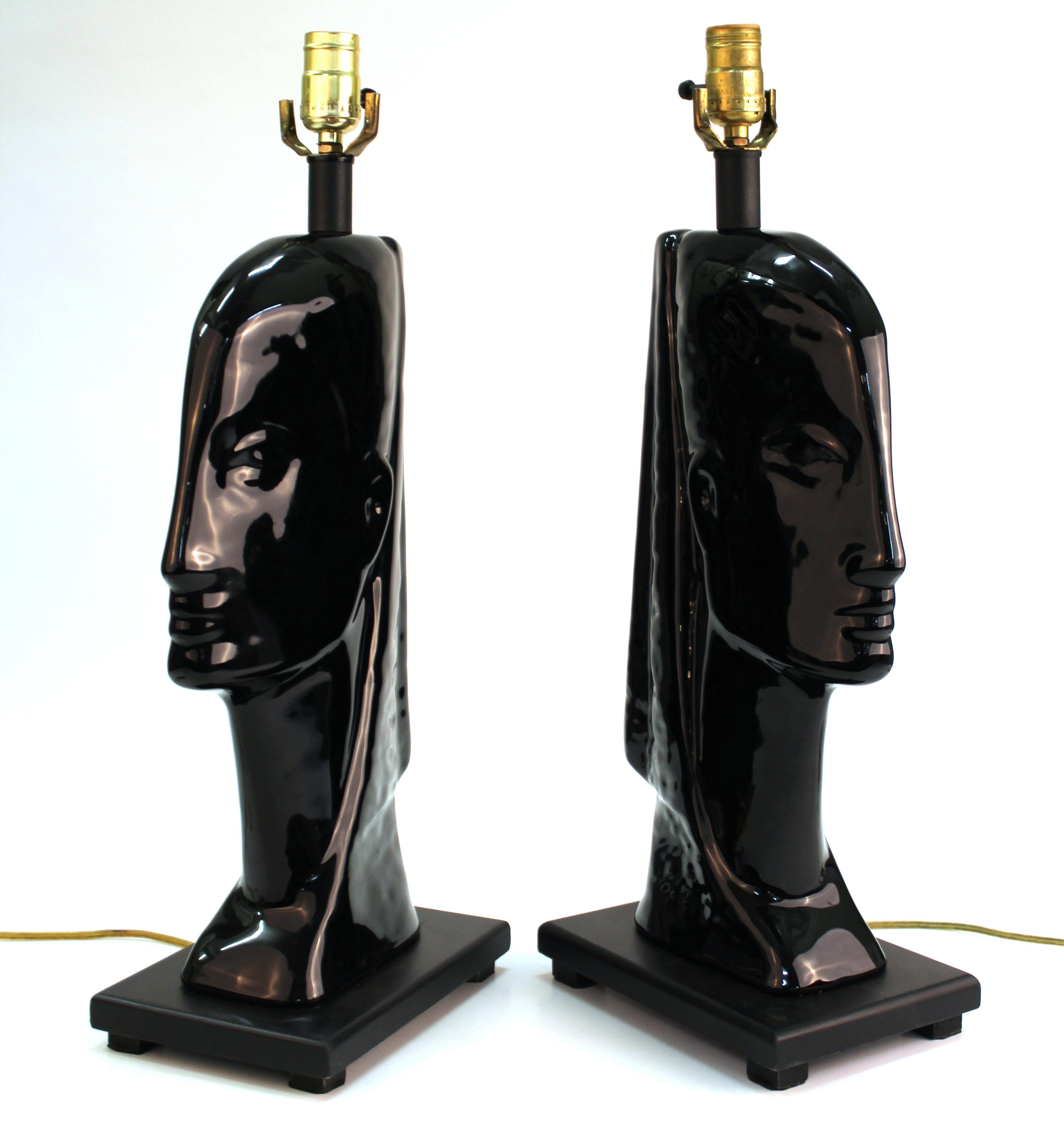 Mid-Century Modern pair of table lamps in the shape of female heads made in black ceramic and mounted on wooden bases. The pair is in great vintage condition with age-appropriate wear.