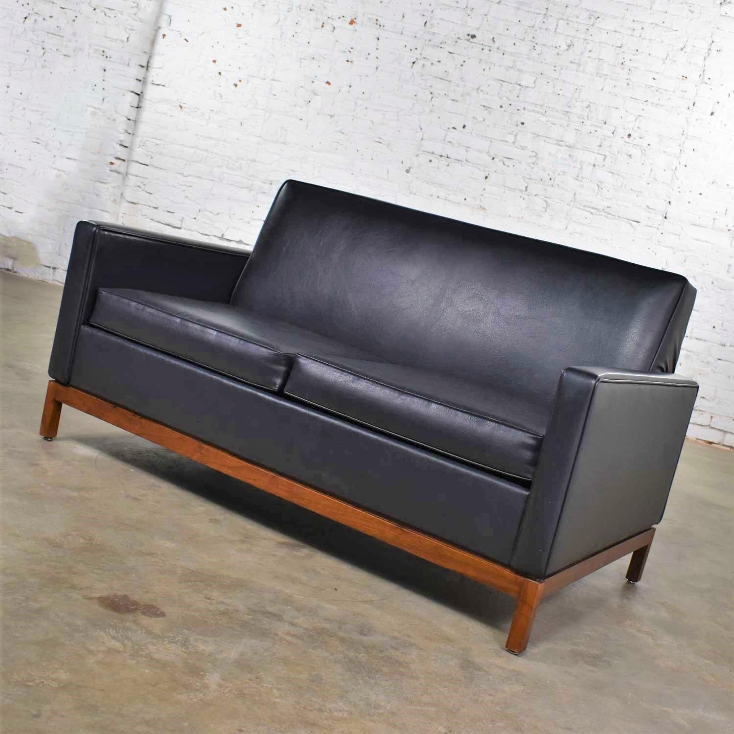 Handsome Mid-Century Modern love seat length sofa in black vinyl faux leather upholstery and walnut base in the style of Wormley for Dunbar or Harvey Probber. It is in wonderful vintage condition. We believe the black vinyl to be fairly new. The