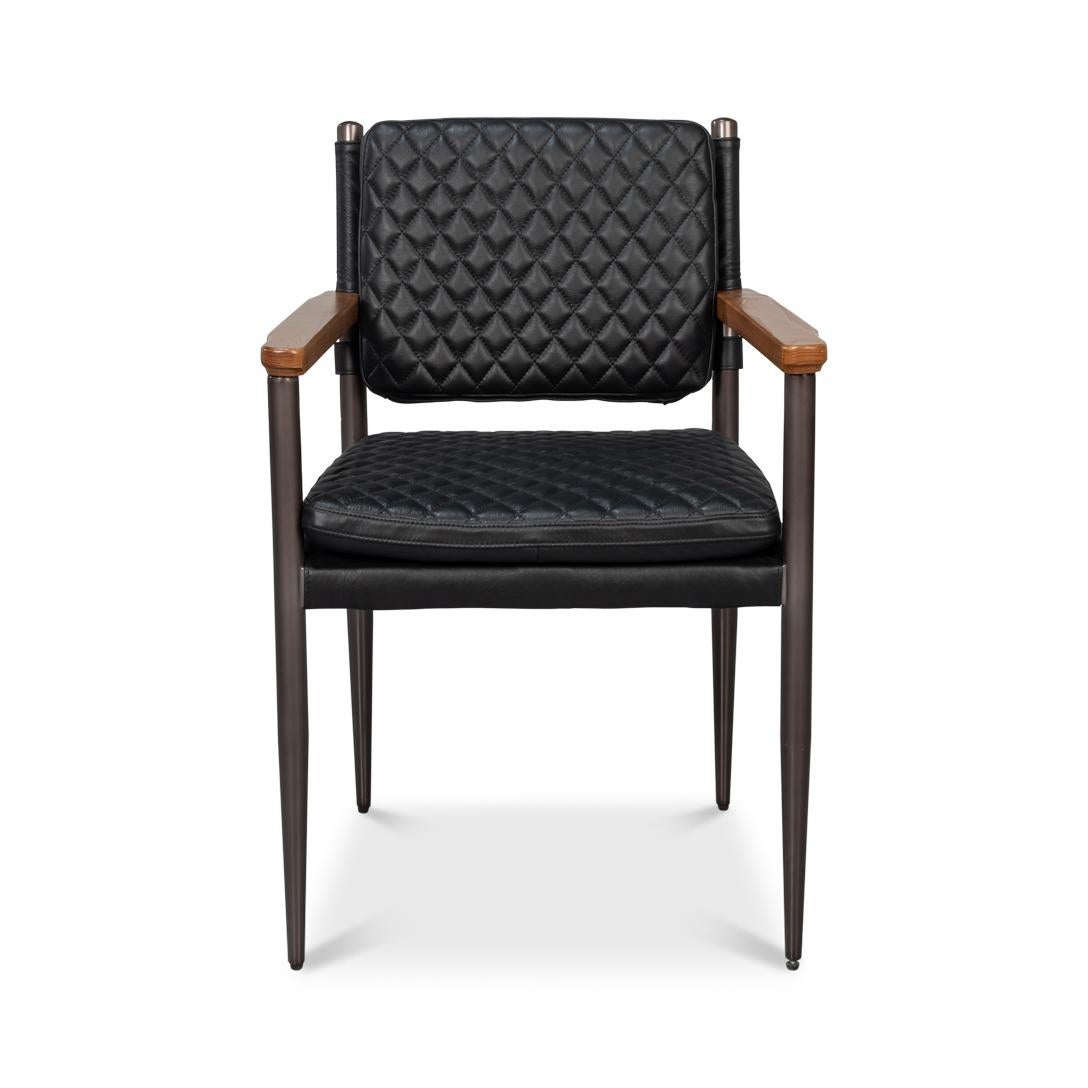 Le revêtement matelassé en cuir noir onyx offre une texture sophistiquée, tandis que le cadre métallique fin et les accoudoirs en bois chaleureux soulignent la silhouette élégante de la chaise. 

Les pieds fuselés soulignent son influence