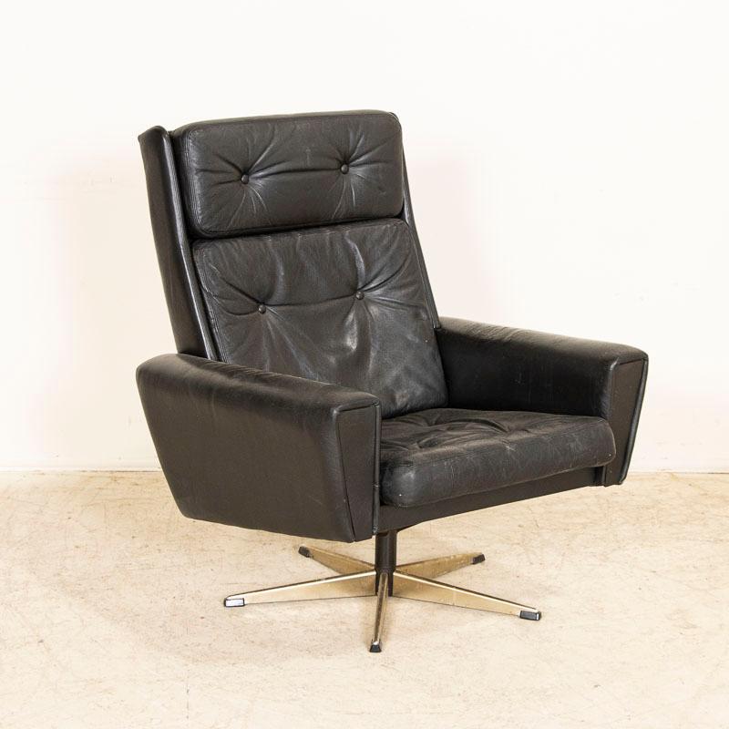 A fun find, this Mid-Century Modern swivel arm chair is great for home or office. It features a padded high back and arms, rotating on a chrome base. The original black leather shows typical age related wear including fading, crackles, creases,