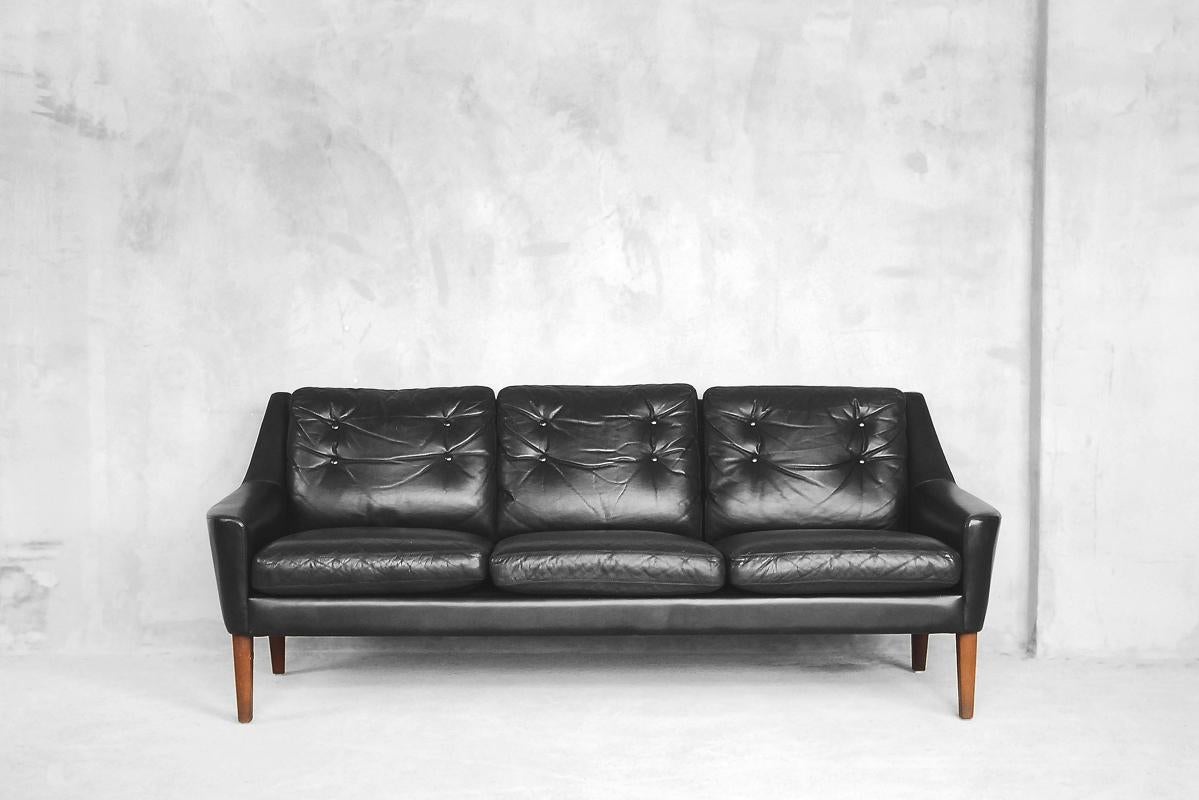 This fabulous Scandinavian elegant sofa in black genuine leather features removable cushions on the seat and backrest. The frame is characteristically raised on wooden legs made of teak. It was manufactured in Sweden by Ulferts Tibro in the early