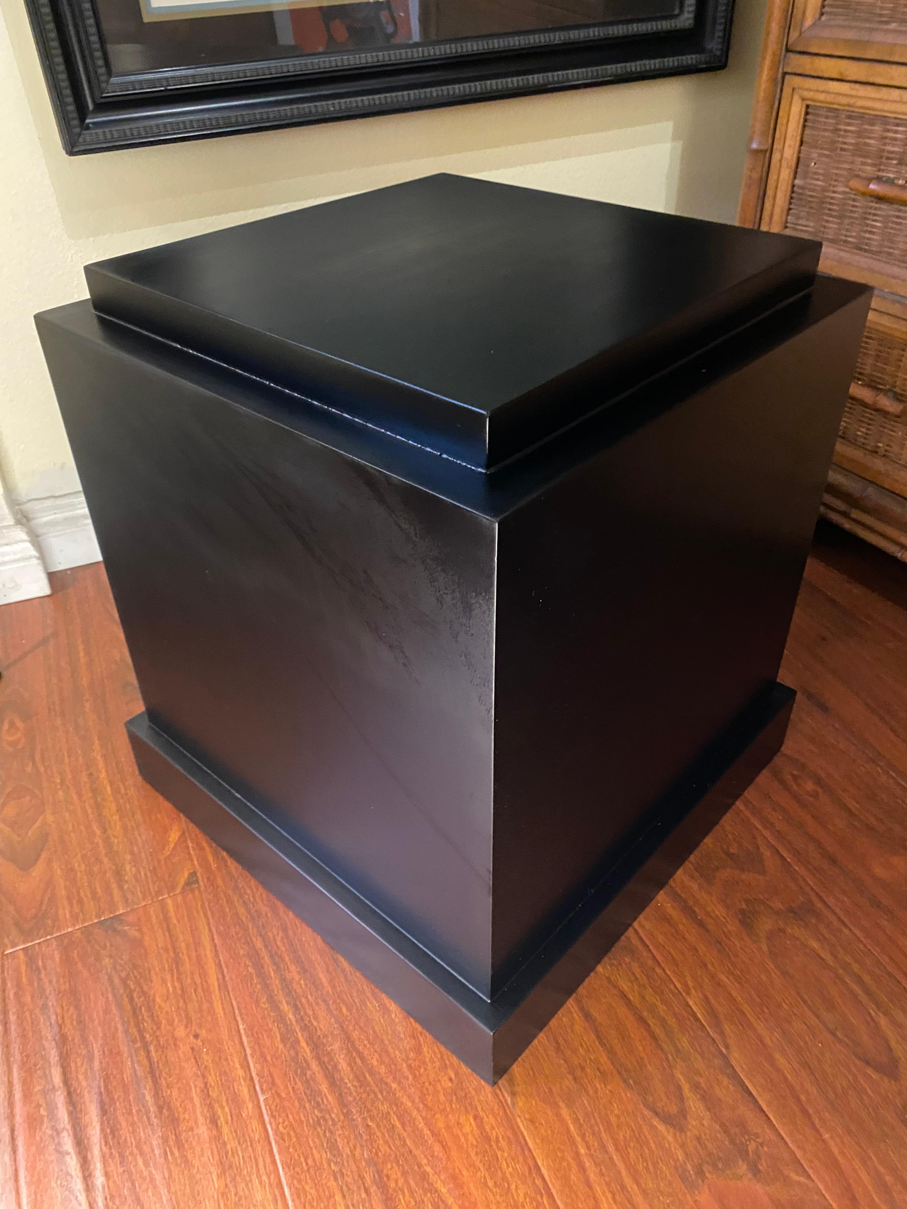 Este pedestal moderno de mediados de siglo lacado en negro presenta un diseño cuadrado bajo con una base ligeramente más ancha para mayor estabilidad y una parte superior más estrecha que resalta la pieza expuesta. Sus líneas limpias y su suave