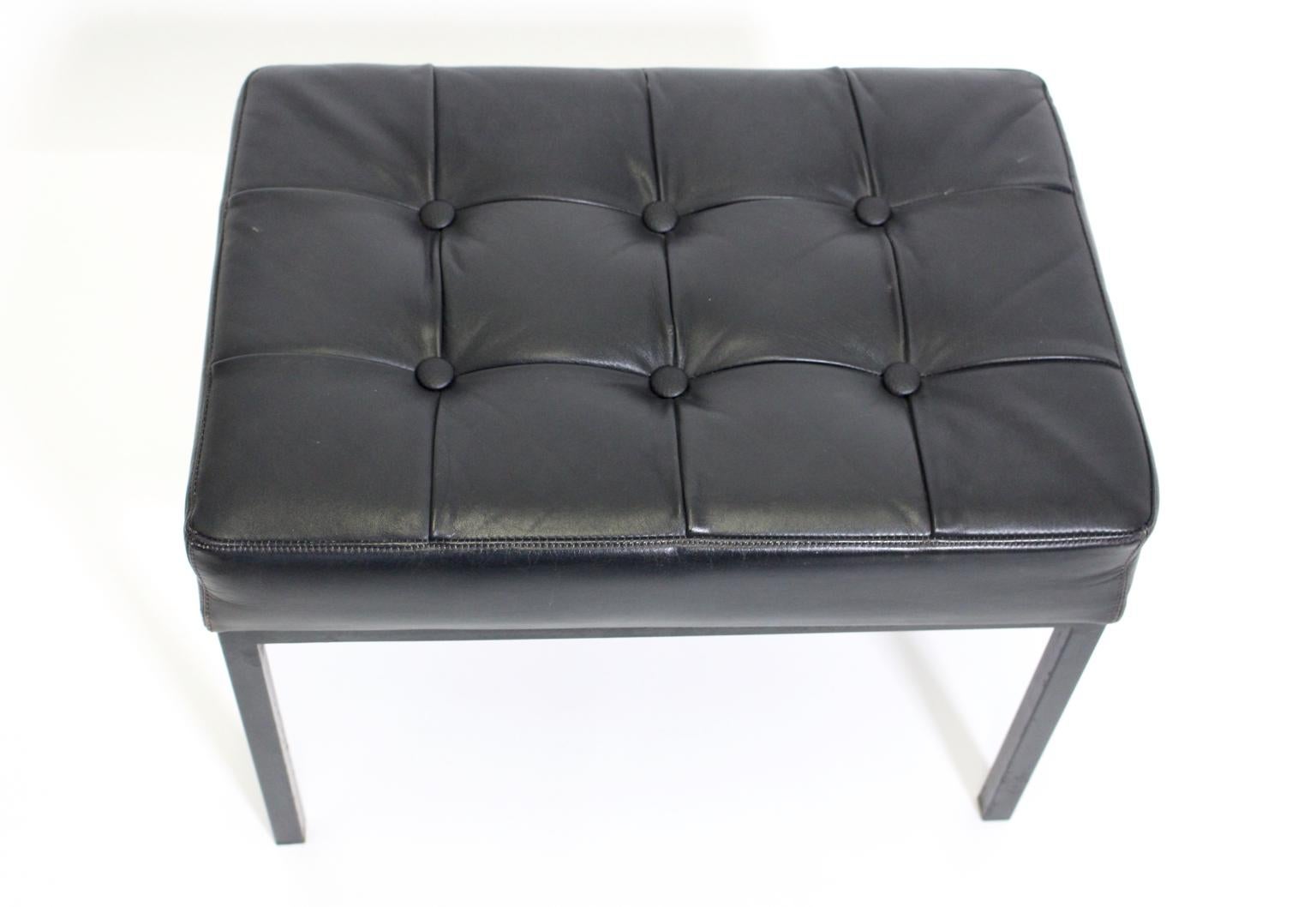 This vintage stool from the 1970s shows a black stitched leather covering. Also the stool is decorated with leather buttons.
The base and the feet were made of black lacquered metal. 
The vintage condition is very good and shows signs of age and