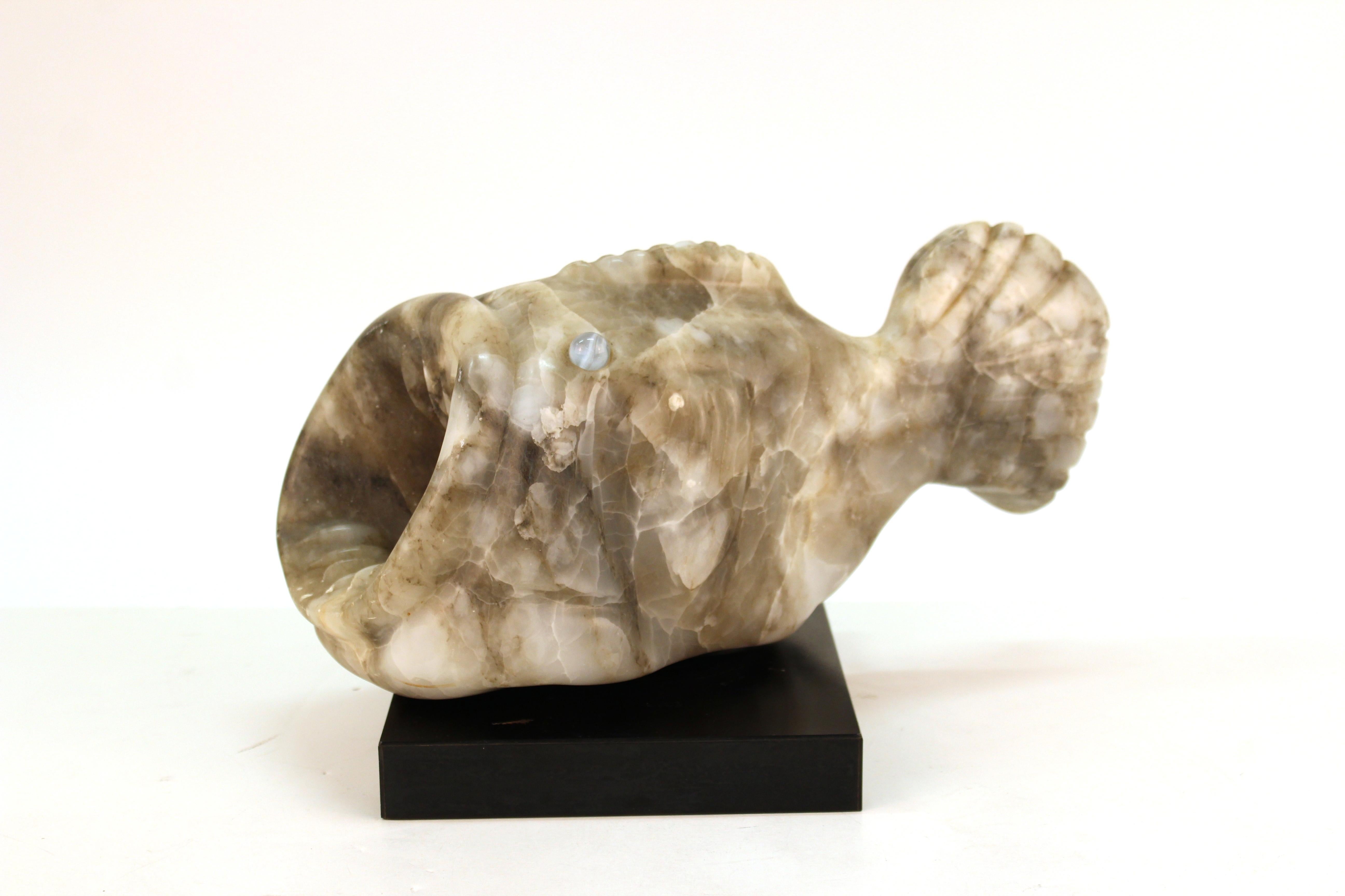 A Mid-Century Modern sculpture of a blowfish with its mouth wide open, sculpted in white stone, with two glass marble eyes. The sculpture sits atop a black square base and was likely made in the United States during the mid-20th century. Some light