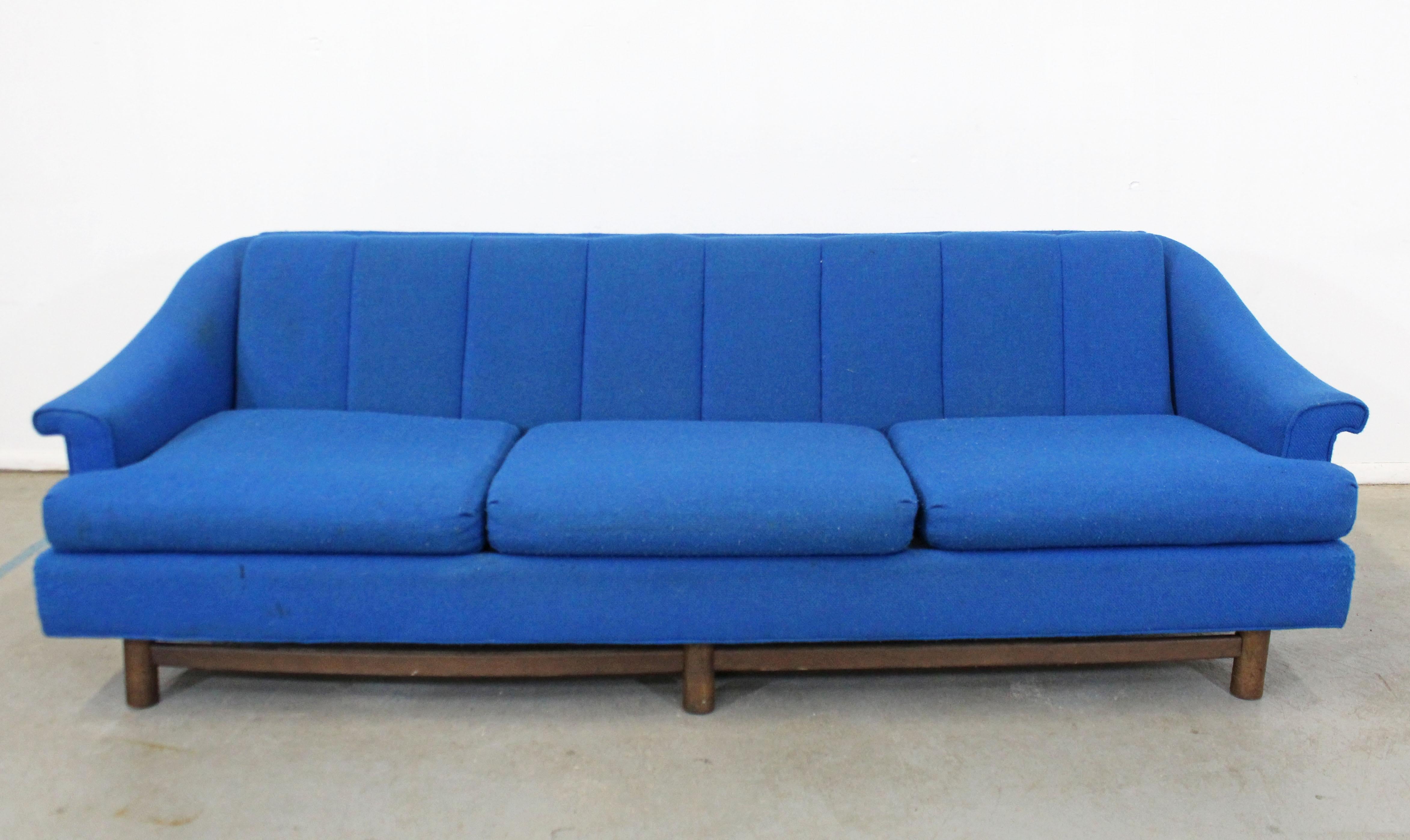 Offered is a vintage Mid-Century Modern sofa on a wooden base with three seat cushions. The cushioning is in good condition, but needs to be reupholstered. The sofa is structurally sound with some surface scratches on the wood. It is not