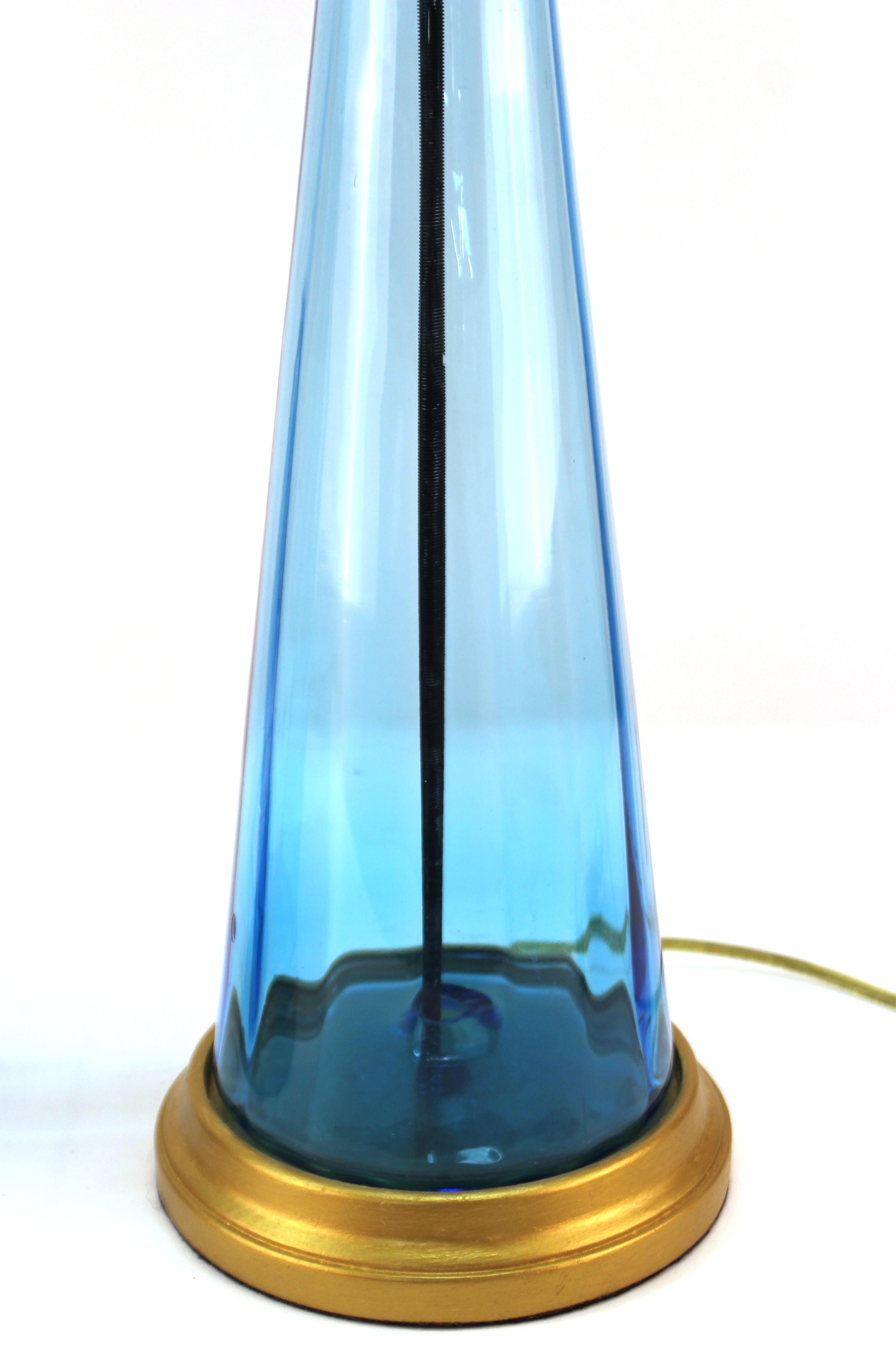 Mid-Century Modern pair of table lamps with a clear blue glass body atop a round giltwood base. The pair was likely made in the mid-20th century and is in great vintage condition.